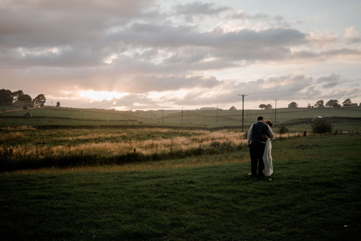 A couple silhouetted against a dramatic sunset sky standing in a grassy meadow during an outdoor photo session.