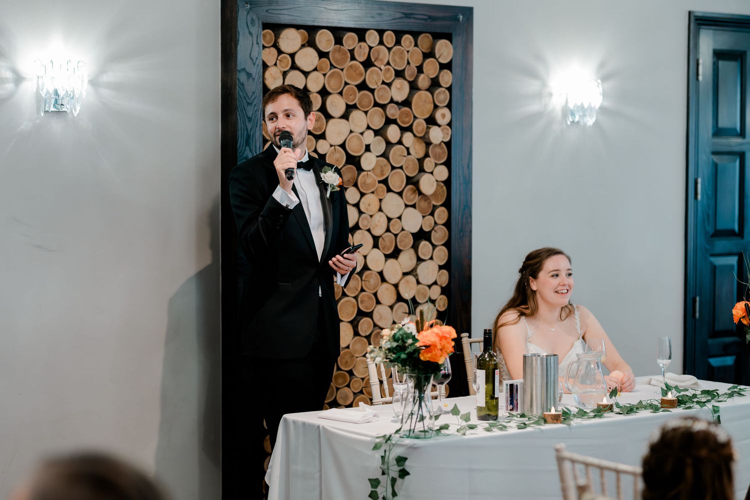 Wedding reception guests celebrate and dance together in an elegant venue decorated with stacked firewood and chandeliers.