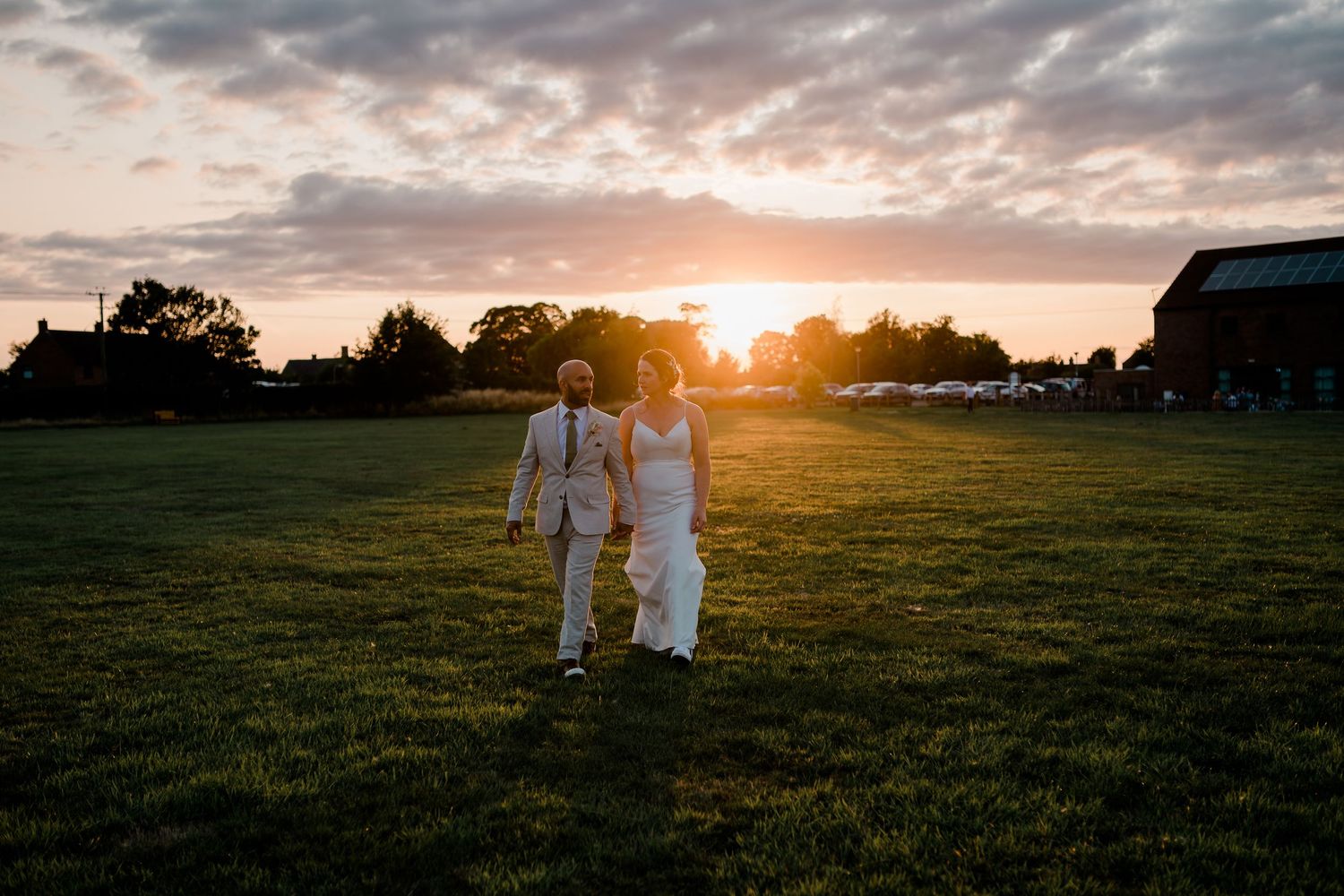 Sunset silhouettes of wedding party walking across grassy field with dramatic sky.