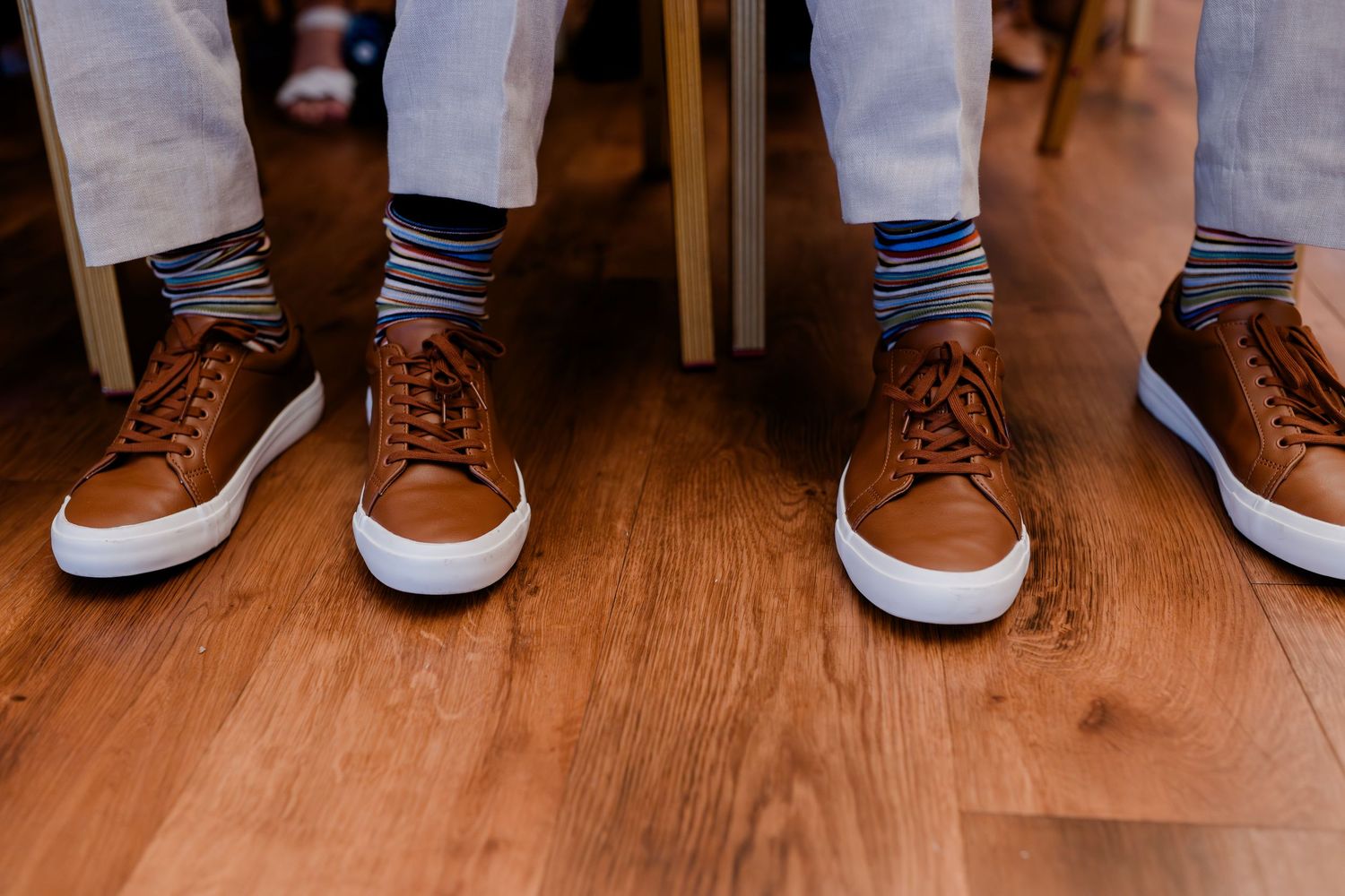 Row of wedding guests' feet and shoes lined up against wooden floor showing diverse footwear styles.