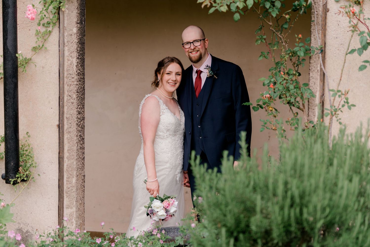 Smiling bride and groom pose together in a charming garden doorway on their wedding day.