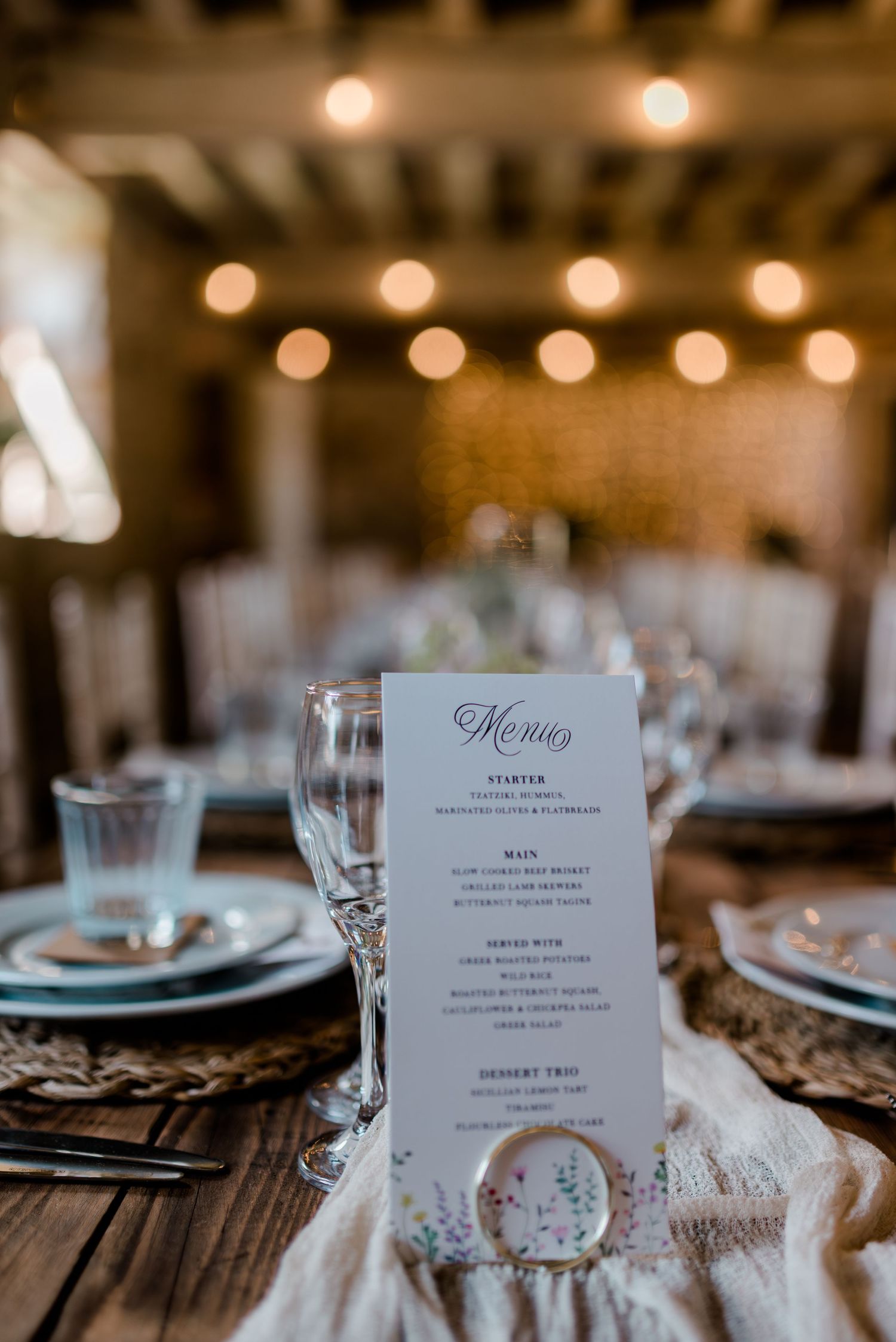 Elegant table settings with menu cards and string lights in a rustic barn reception venue.