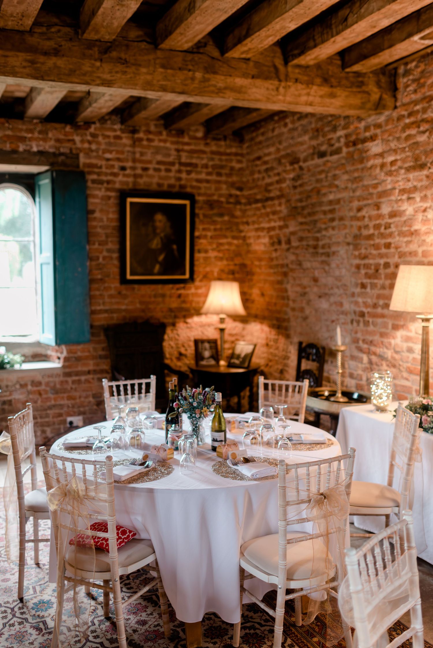 Elegant table setting in rustic brick room with exposed beams and white table linens.
