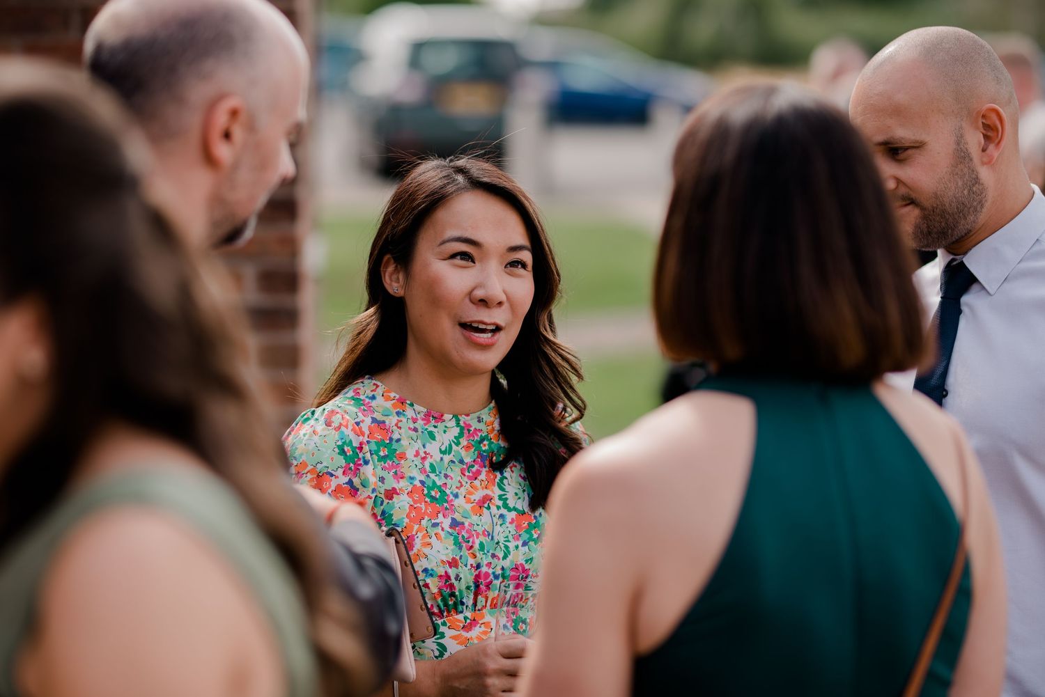 Wedding guests laugh and smile together during an outdoor celebration on a sunny day.