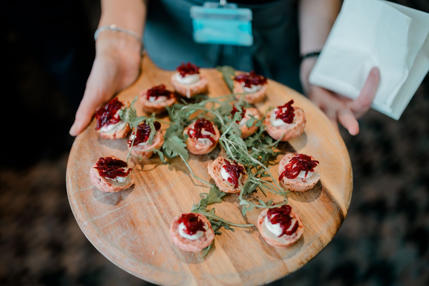 Wooden serving board with elegant appetizers topped with garnishes and red sauce.