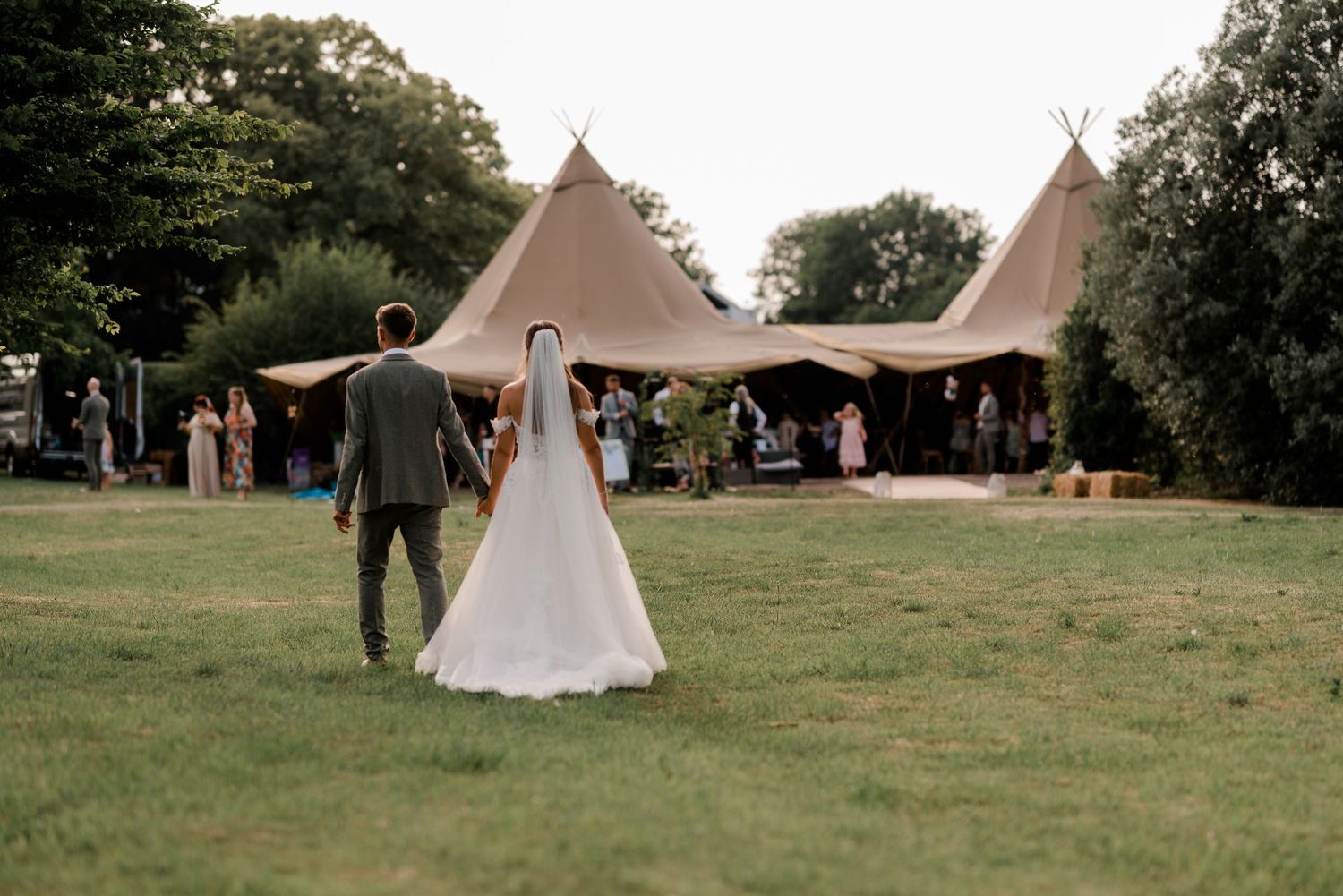 Two beige tipi-style wedding tents set up on a green lawn for an outdoor celebration event.