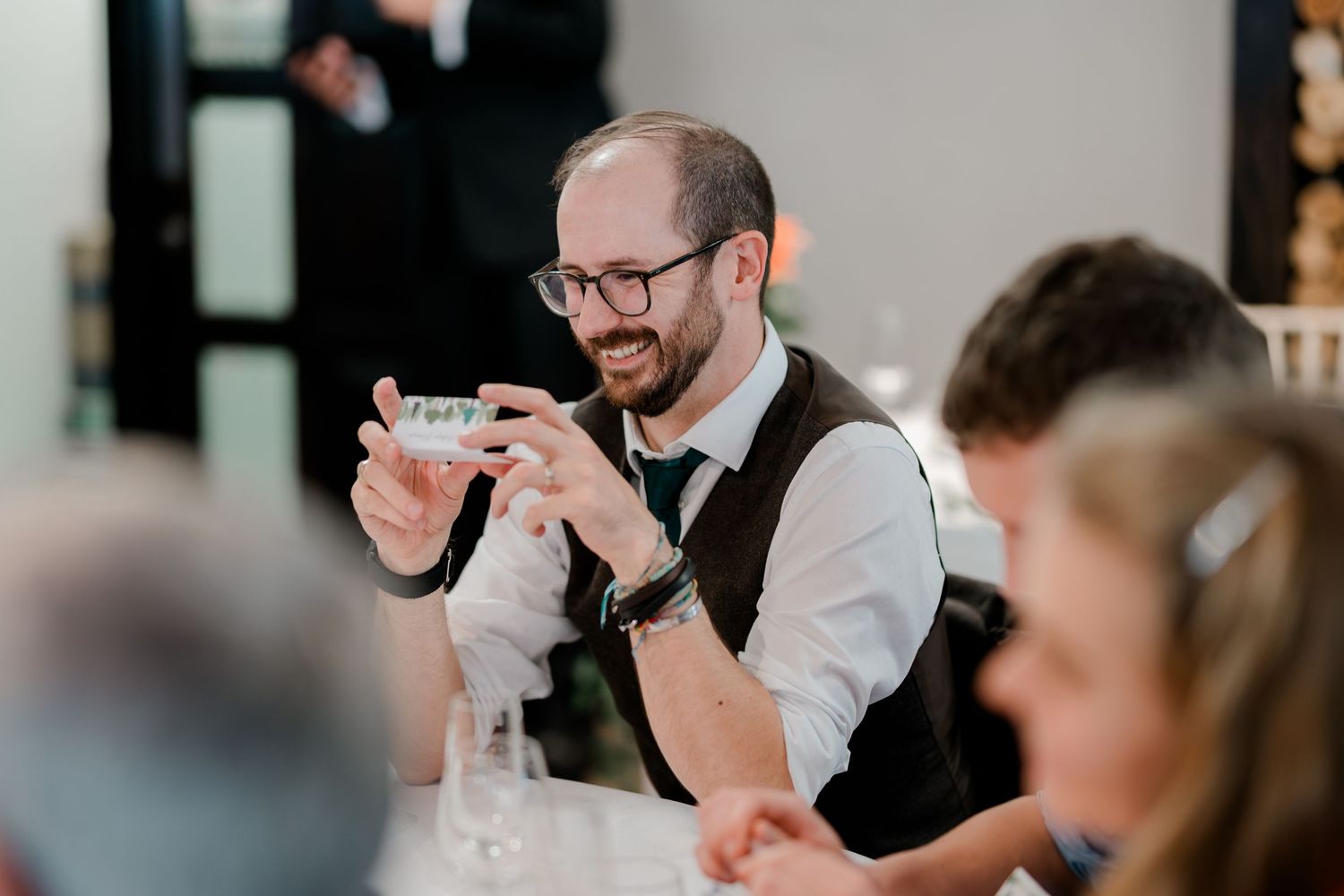 Smiling wedding guest taking a photo with his smartphone during a wedding reception celebration.