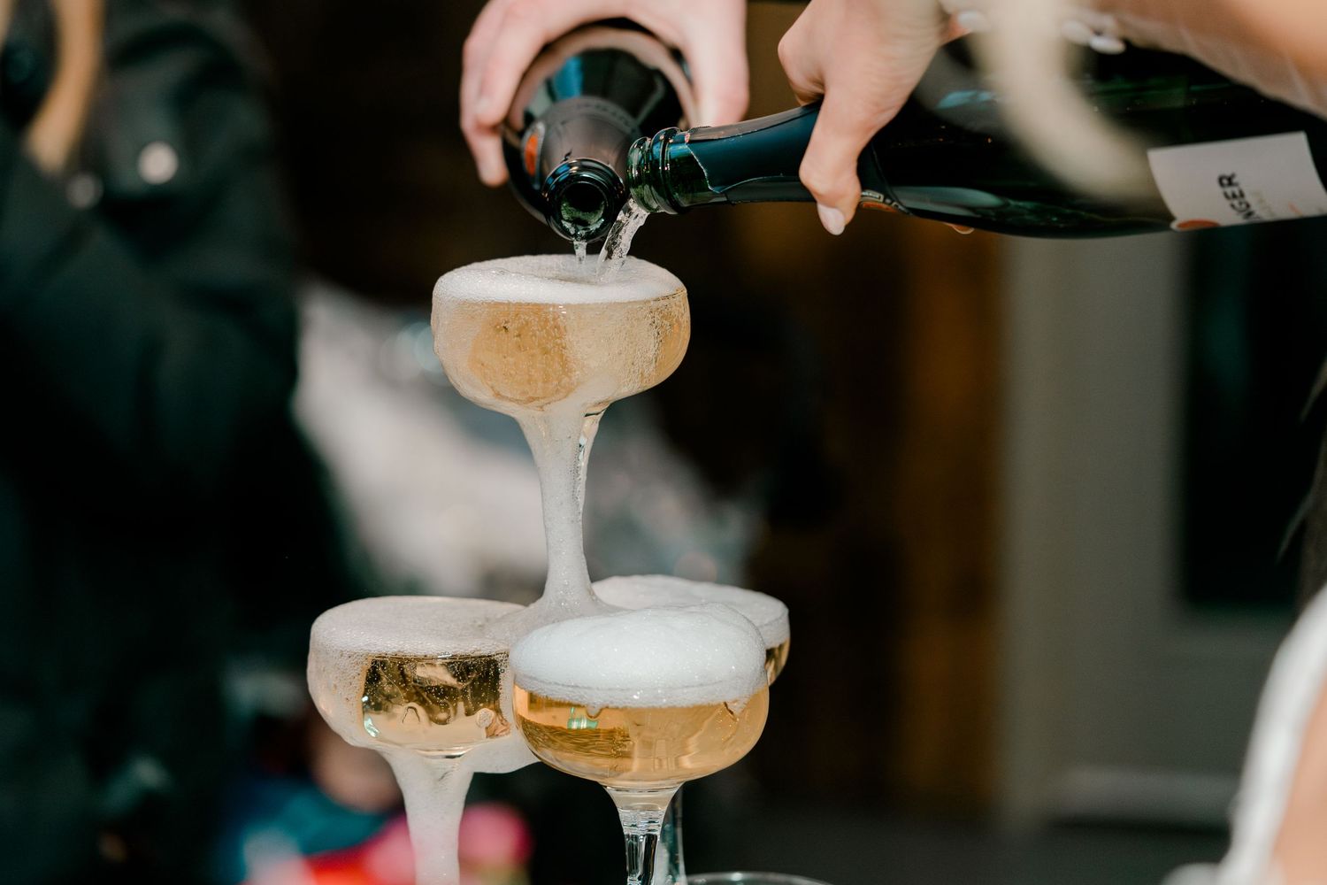 Champagne being poured into elegant coupe glasses forming a sparkling tower at a wedding.