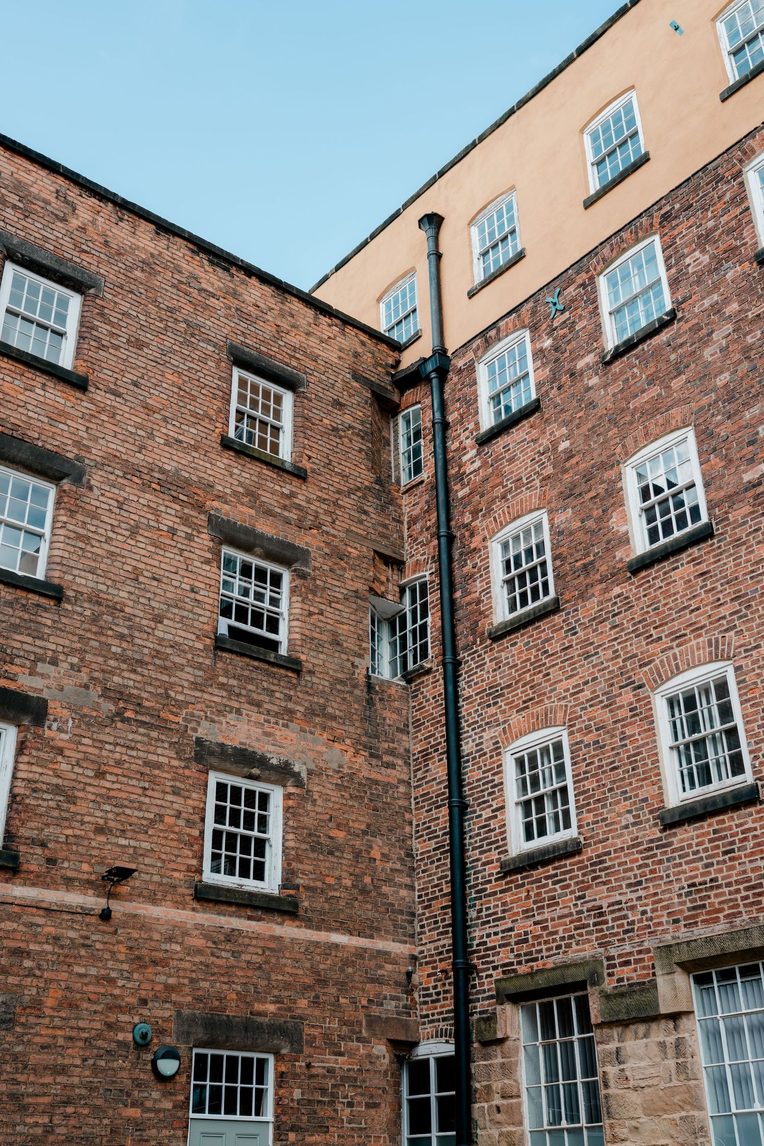 Historic red brick building with white sash windows and a black lamp post against a clear blue sky.