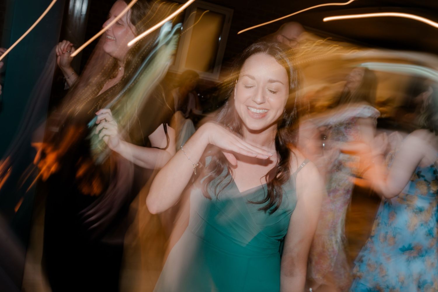 Joyful bridesmaid in teal dress dancing energetically at a lively wedding reception party.