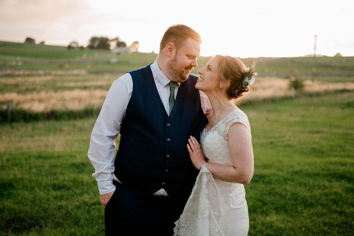 Bride and groom share a tender moment in a golden sunset field.
