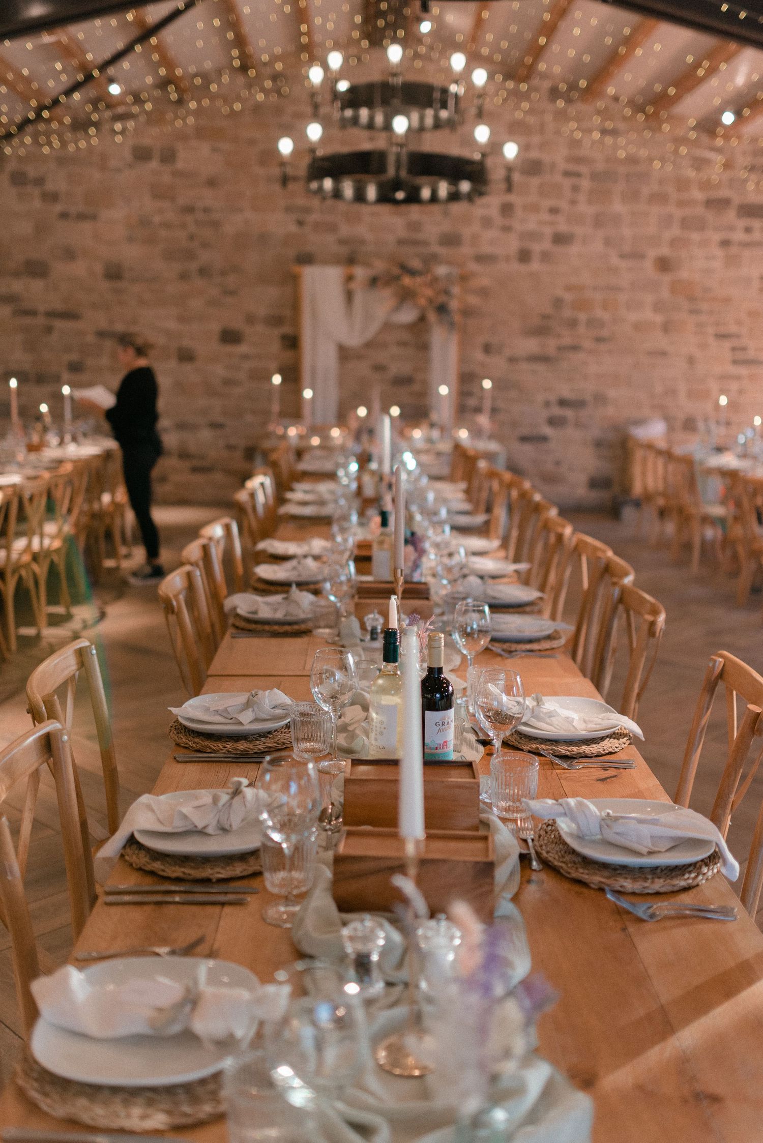 Stunning barn wedding reception with long wooden tables, taper candles, fairy lights and exposed stone walls.
