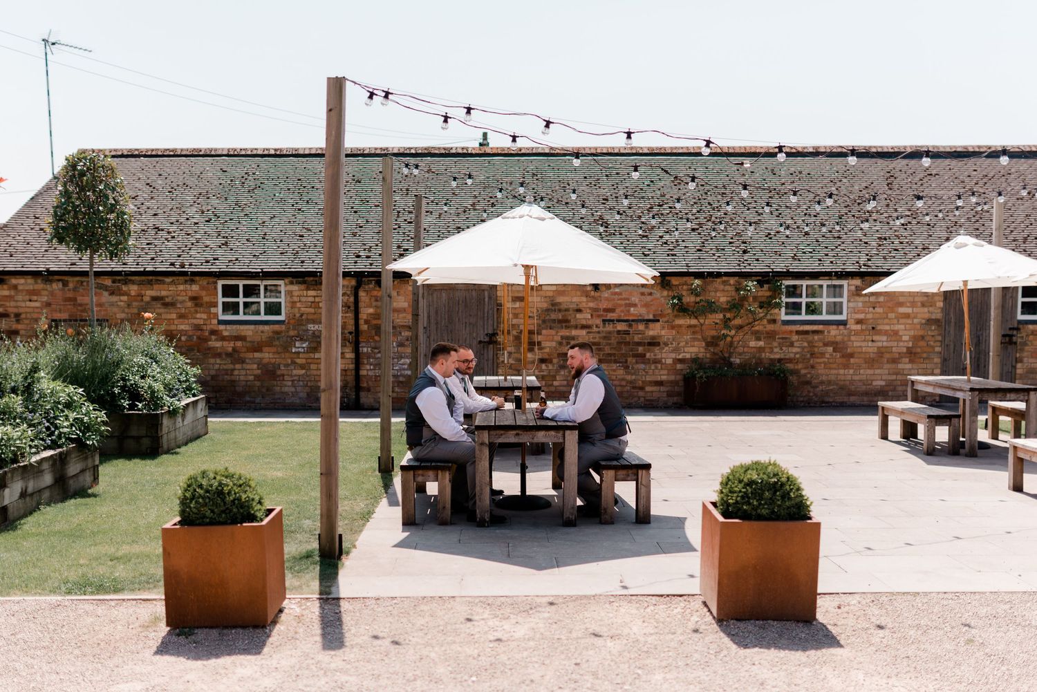 Rustic outdoor venue with brick buildings and planters along a paved walkway.