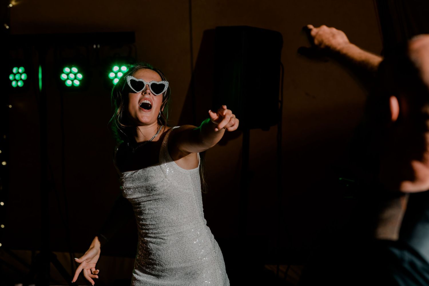 A couple dances joyfully at a wedding reception with colorful lights in the background.