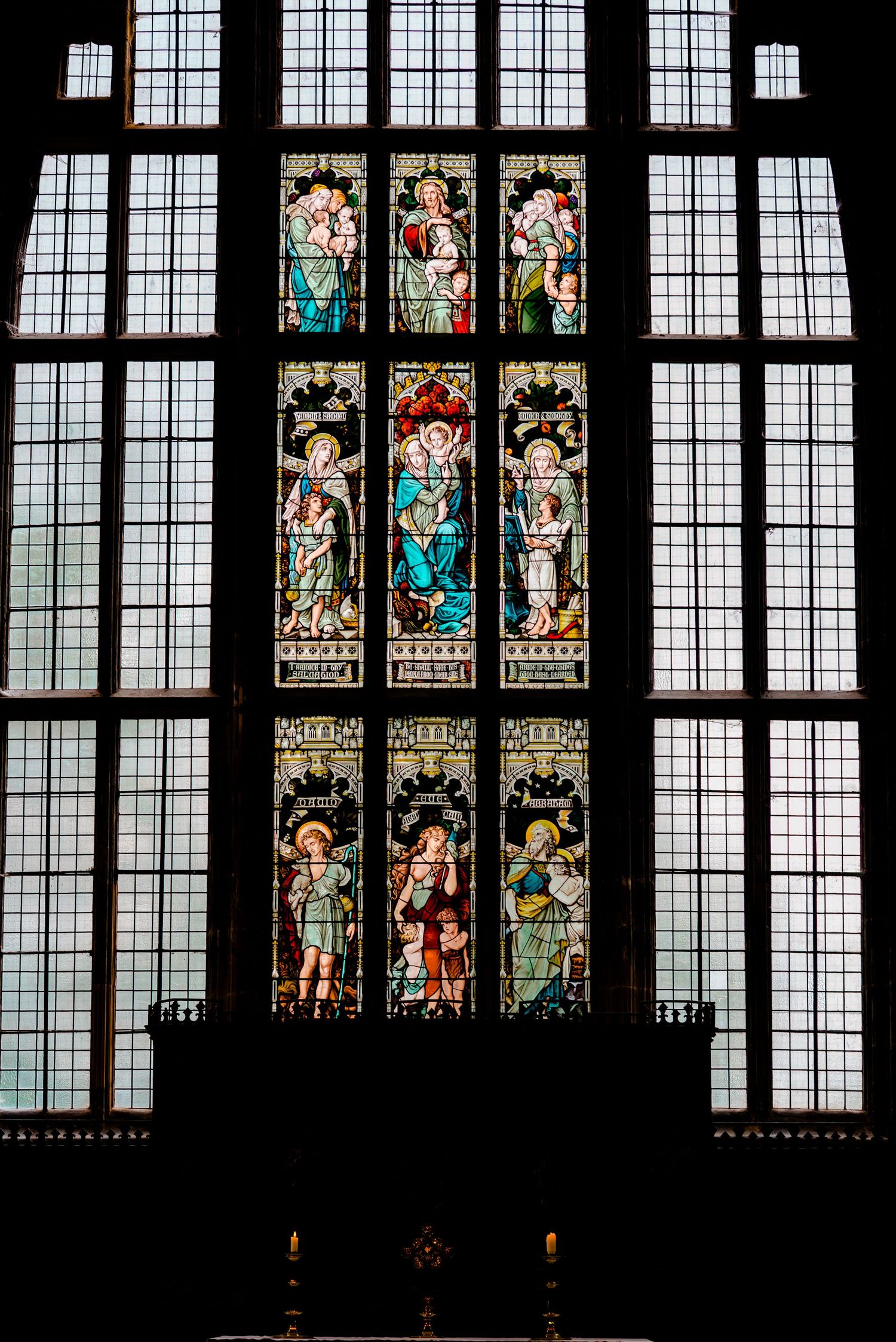 Beautiful stained glass windows with religious motifs in a Gothic church interior with dark framing.