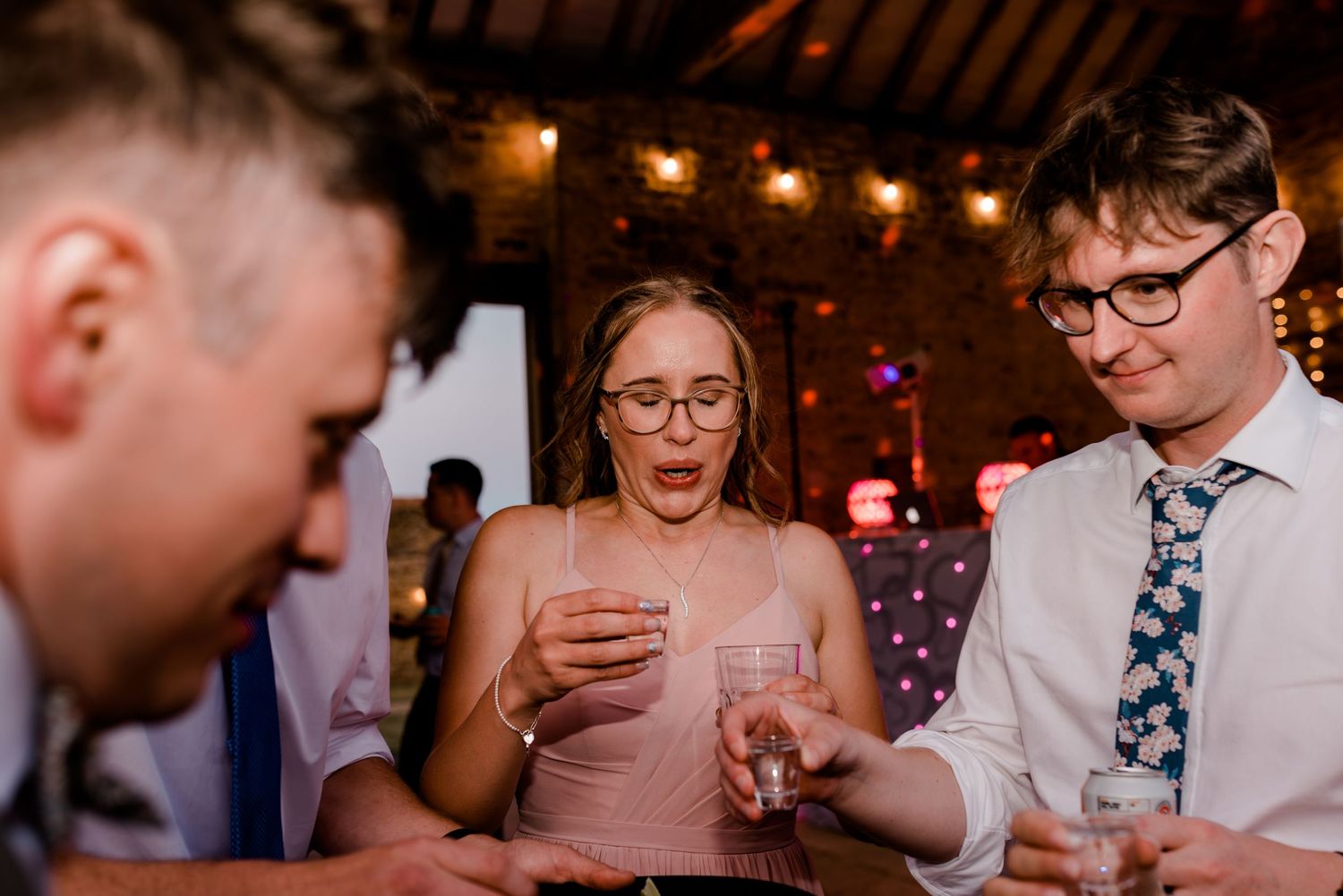Wedding reception guests dancing and enjoying themselves under string lights in a dimly lit venue.