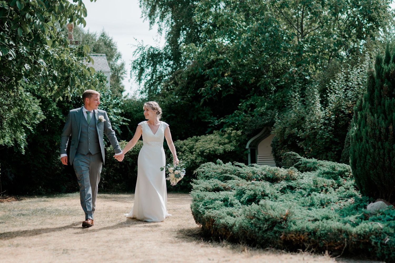 A bride and groom walk hand-in-hand through a lush garden on their wedding day.