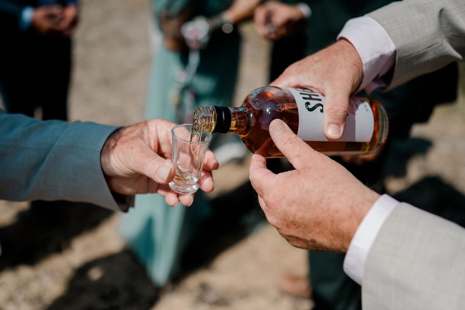 Whisky being poured into a shot glass during an outdoor wedding celebration.