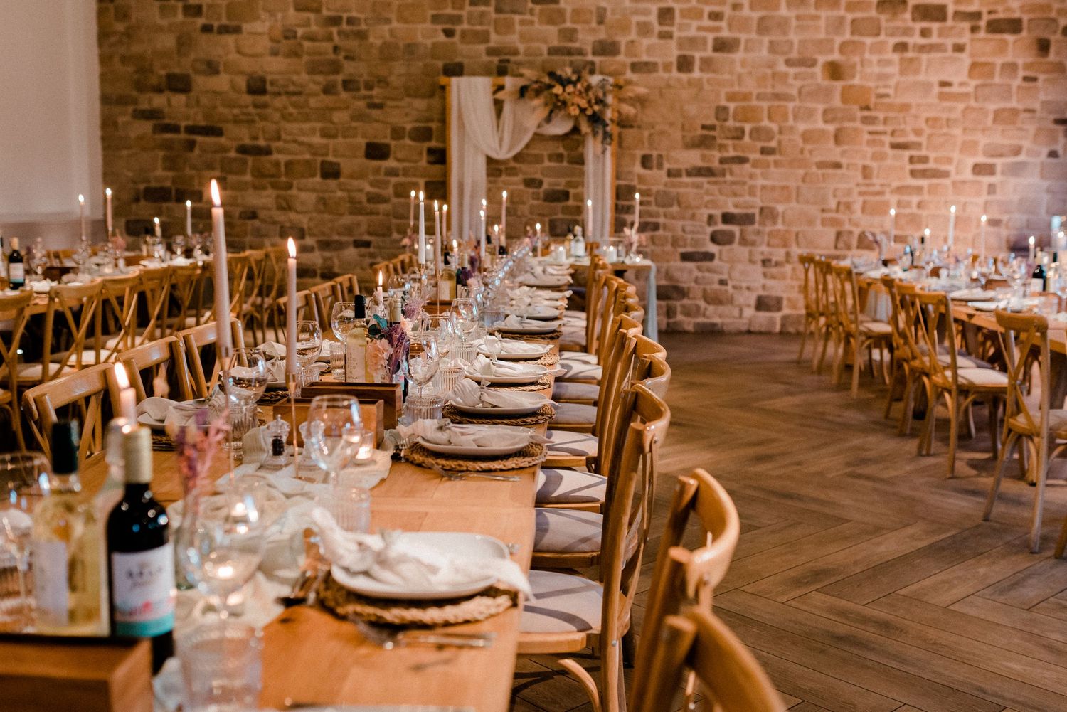 Rustic barn wedding reception with long banquet tables, candlelight, cross-back chairs and exposed brick walls.