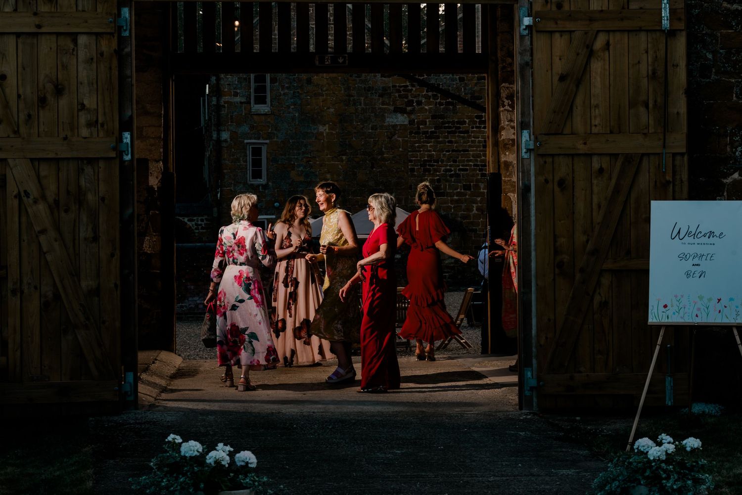 Guests arriving at a rustic barn wedding venue through large wooden doors at dusk.