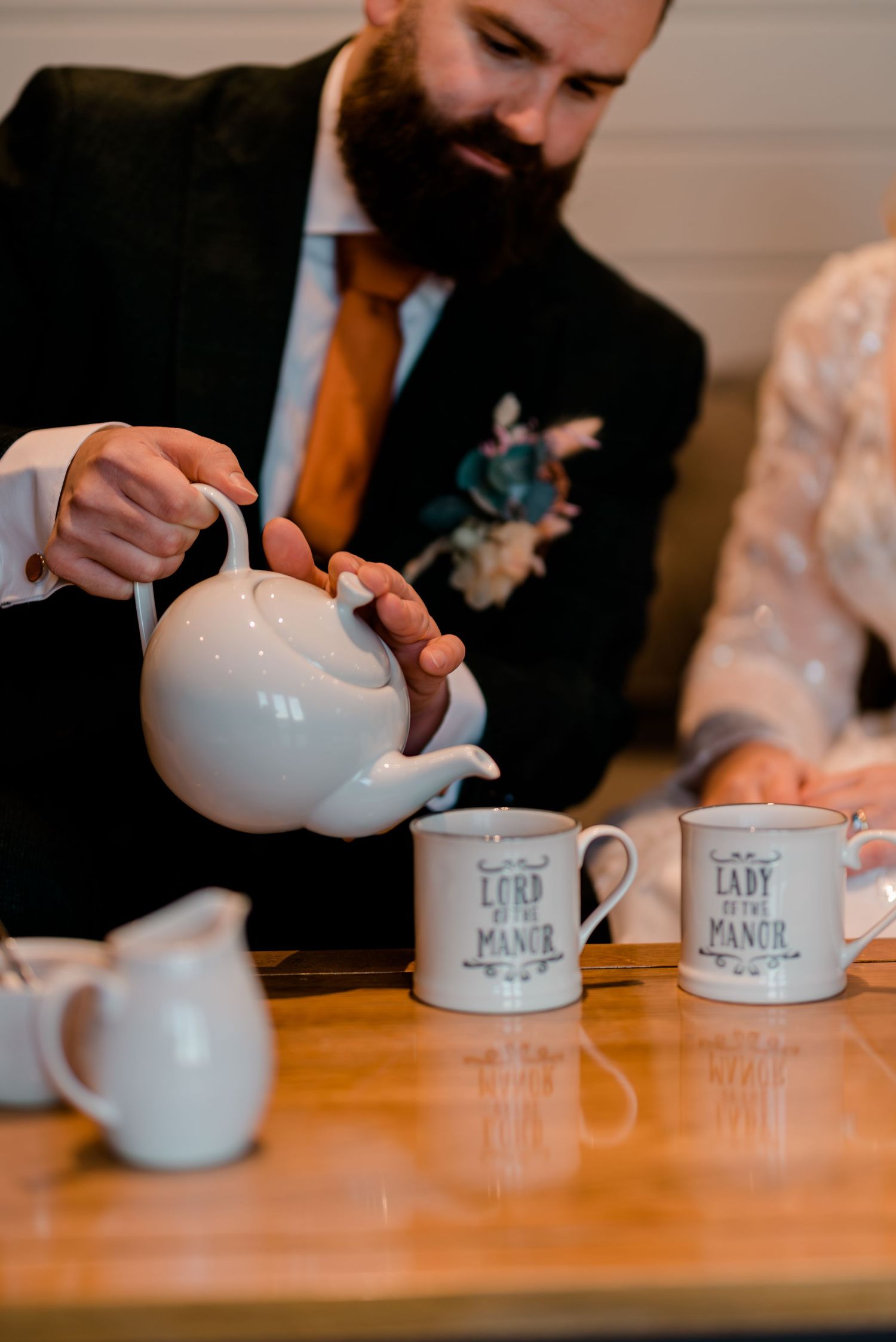 Wedding guest pouring tea from white teapot into custom labeled mugs.