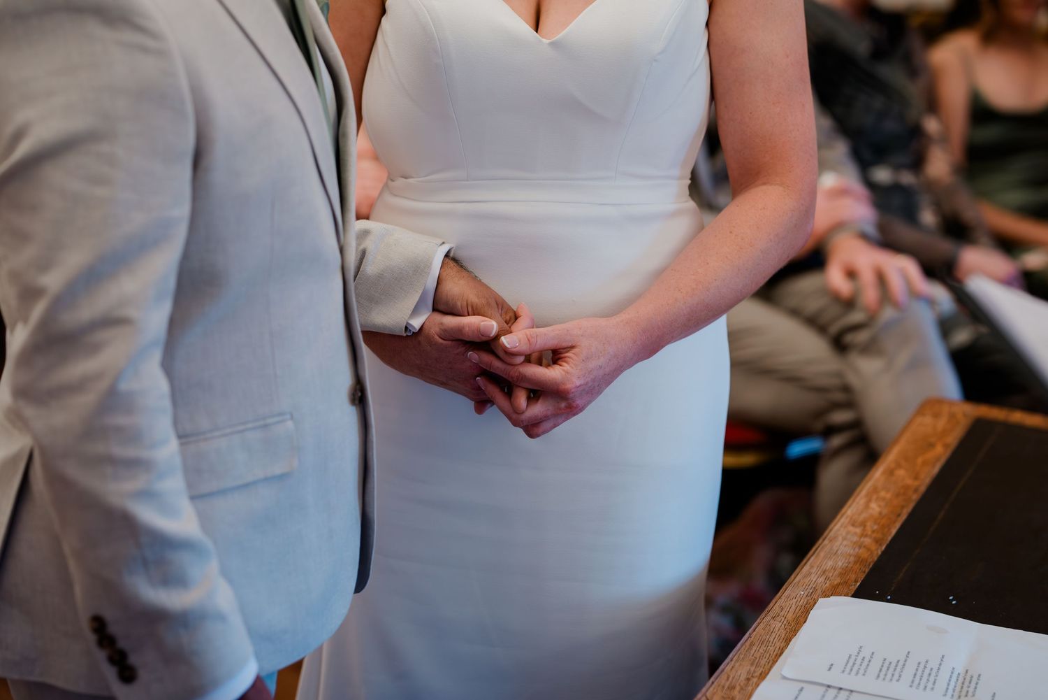 Couple holding hands during outdoor wedding ceremony with guests seated on white chairs.