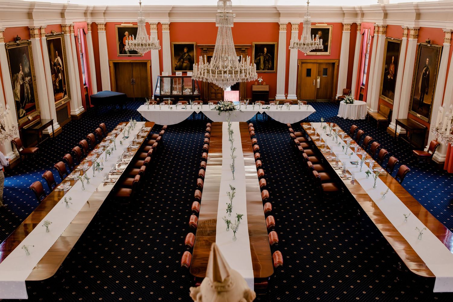 An elegant white event space with black carpeting and crystal chandeliers showcases traditional wedding table settings.