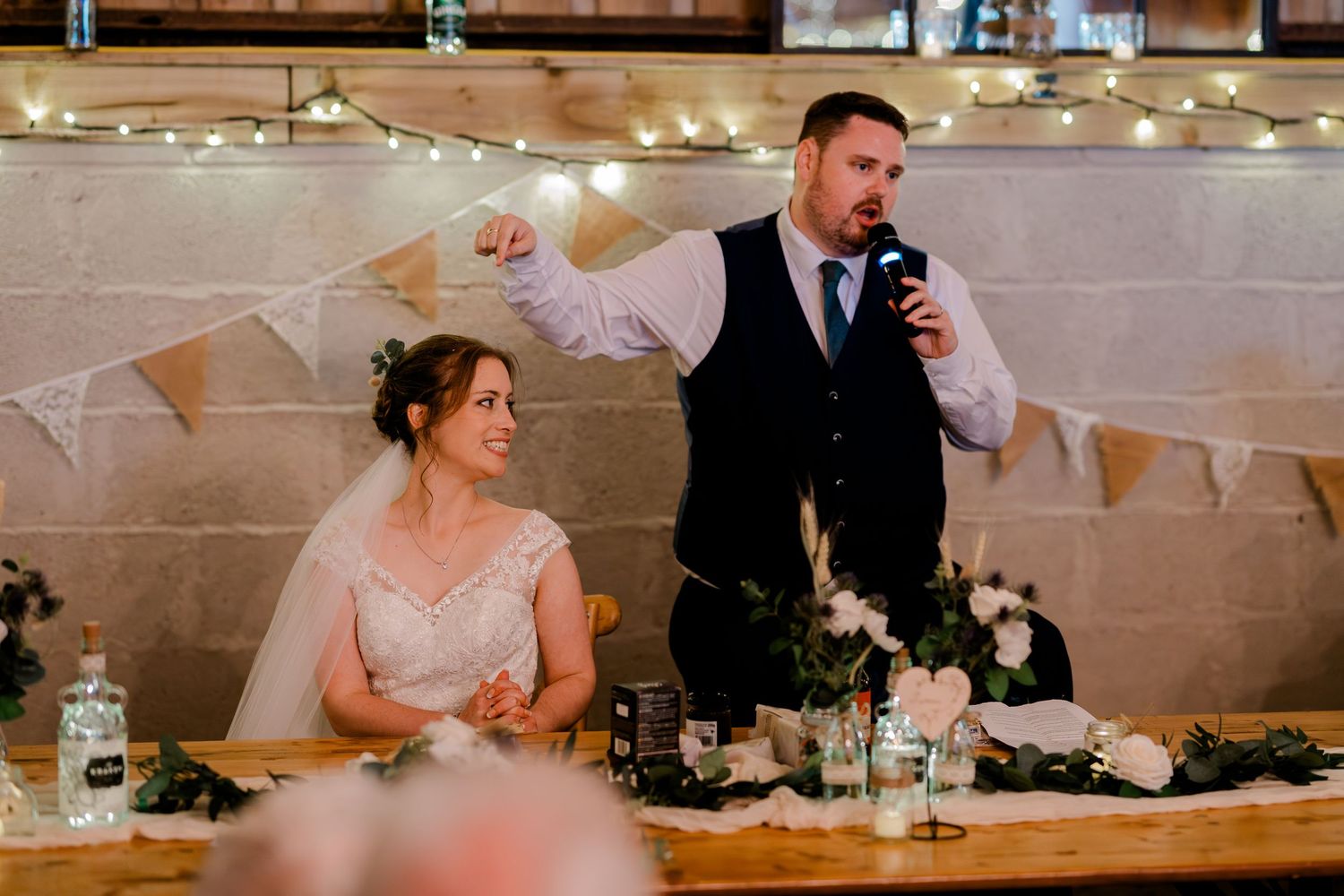 Wedding reception table decorated with rustic bunting flags and string lights in a barn-style venue.