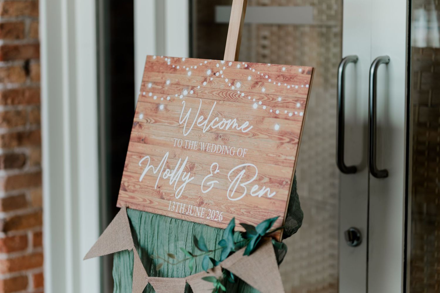 Rustic wooden wedding welcome sign for Molly and Ben decorated with string lights and greenery.