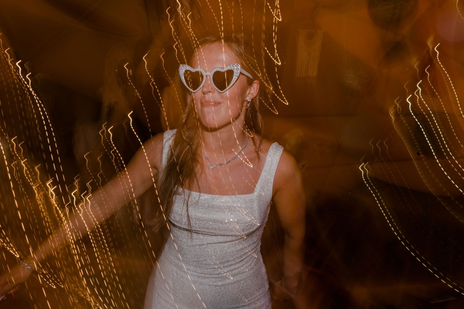 A person in sunglasses stands among golden sun-lit wheat stalks in a field during magic hour.