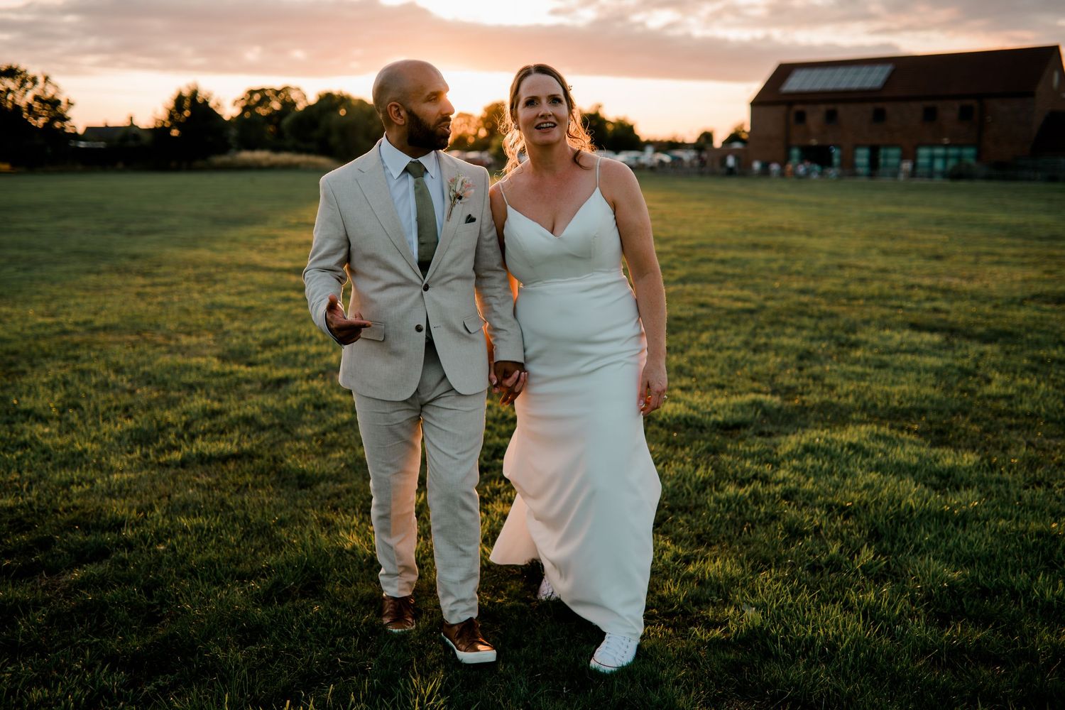 Couple walks across a grassy field during golden hour at their wedding.