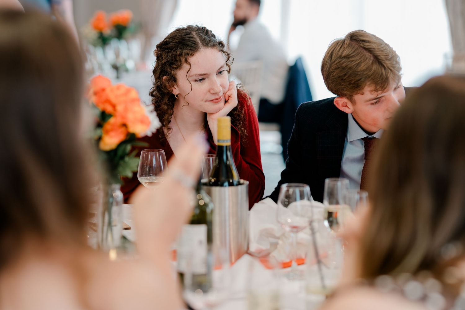 Wedding guests smile and laugh during a joyful reception celebration with orange floral decorations.