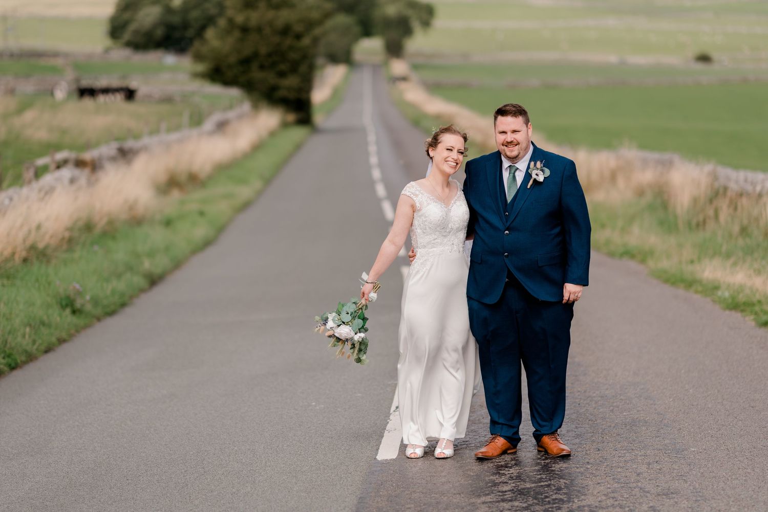 Couple walking together on a scenic country road surrounded by green rolling hills and fields.