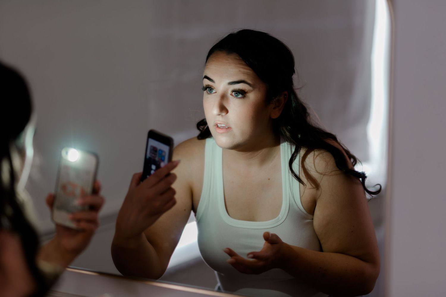 Person in dim lighting looking at bright smartphone screen causing harmful blue light exposure at night.
