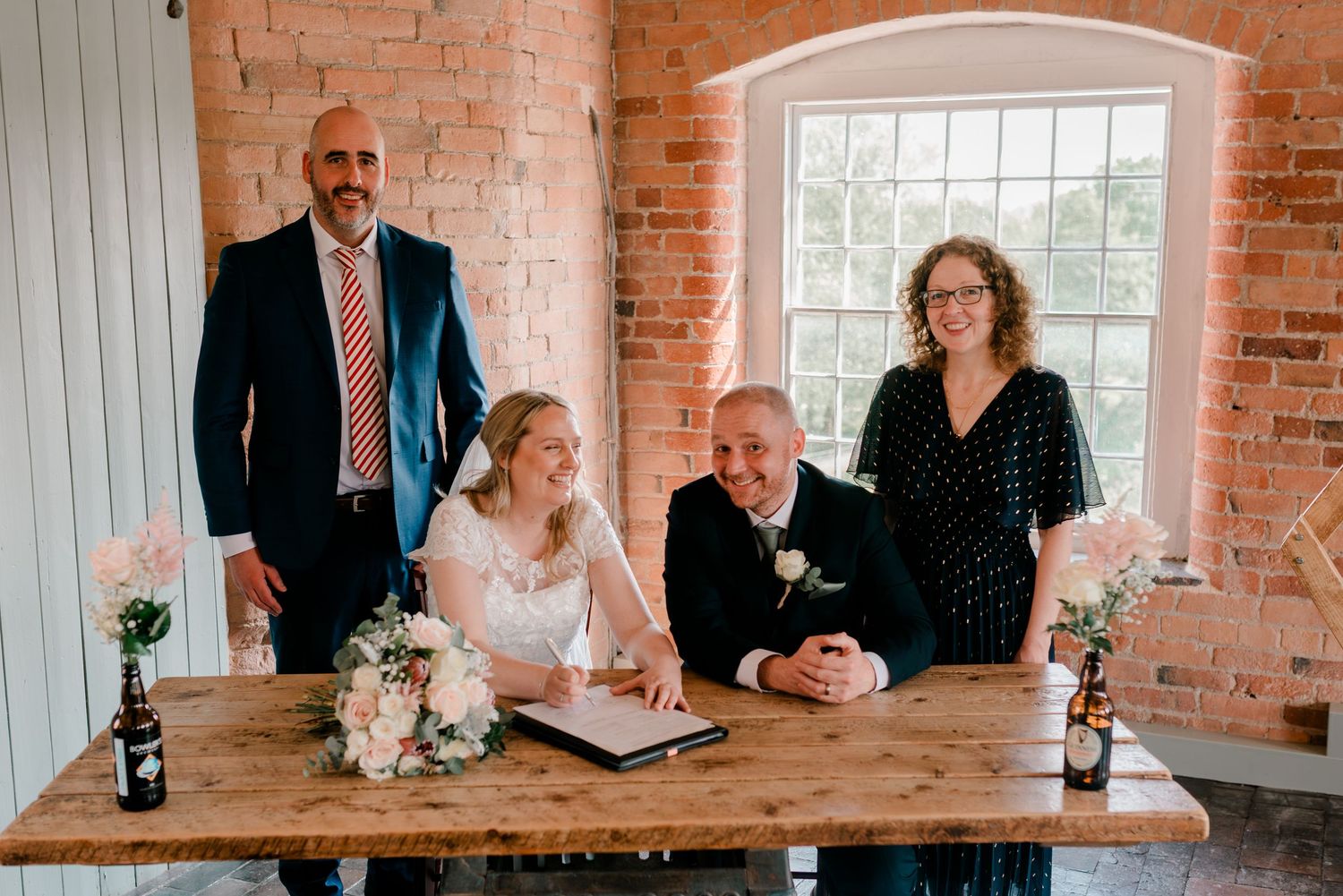 Wedding guests gathered at rustic brick venue sharing drinks and conversation at wooden tables.