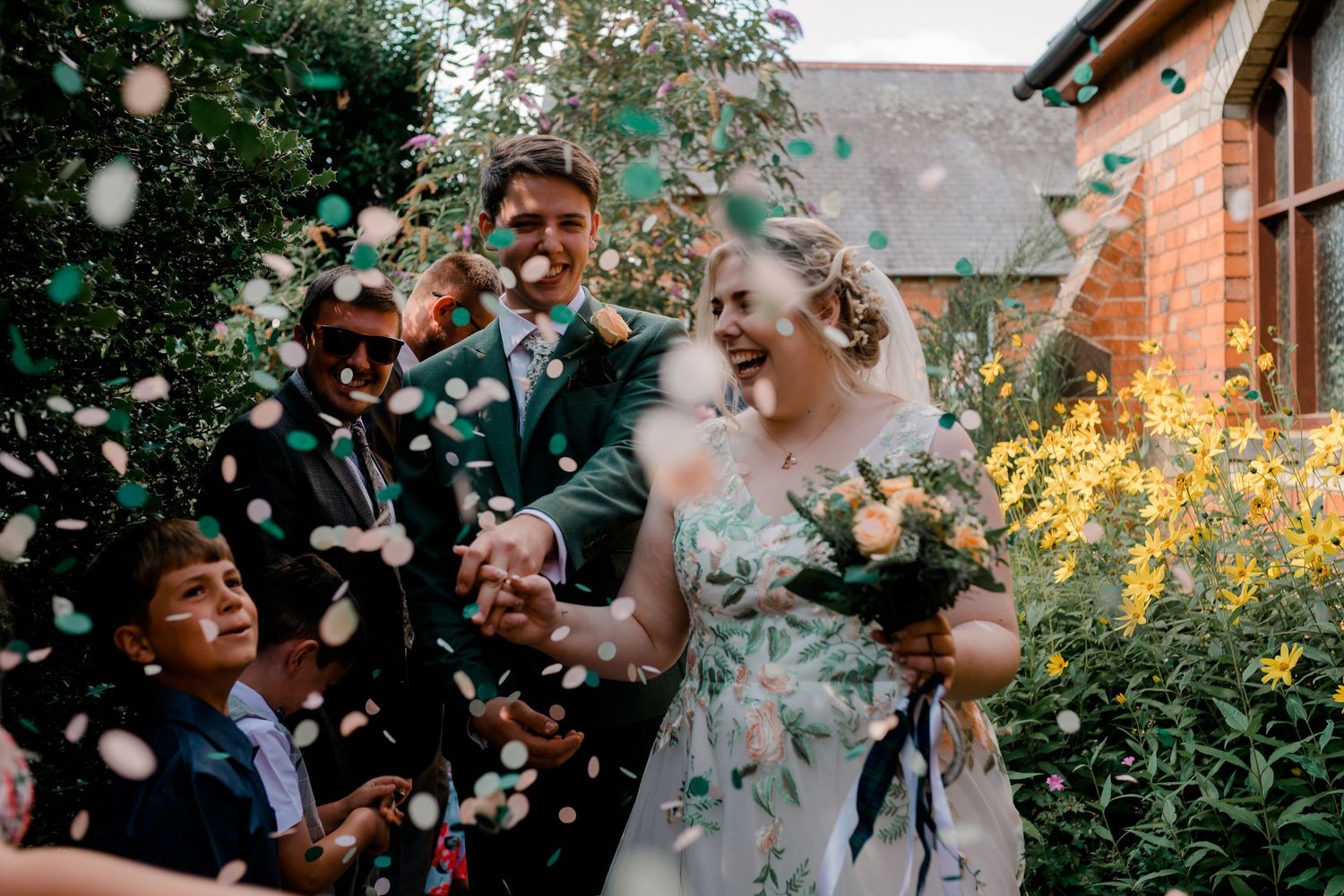 Joyful outdoor wedding celebration with confetti being tossed in a garden setting.