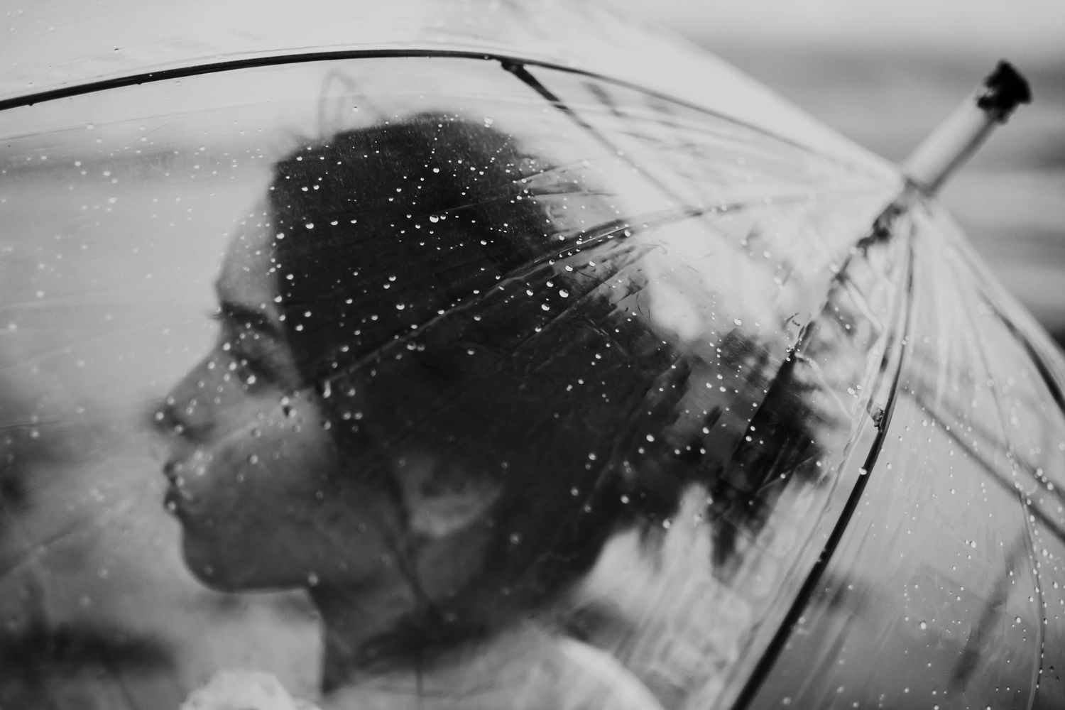Artistic black and white photo of a silhouette behind a rain-covered transparent umbrella.