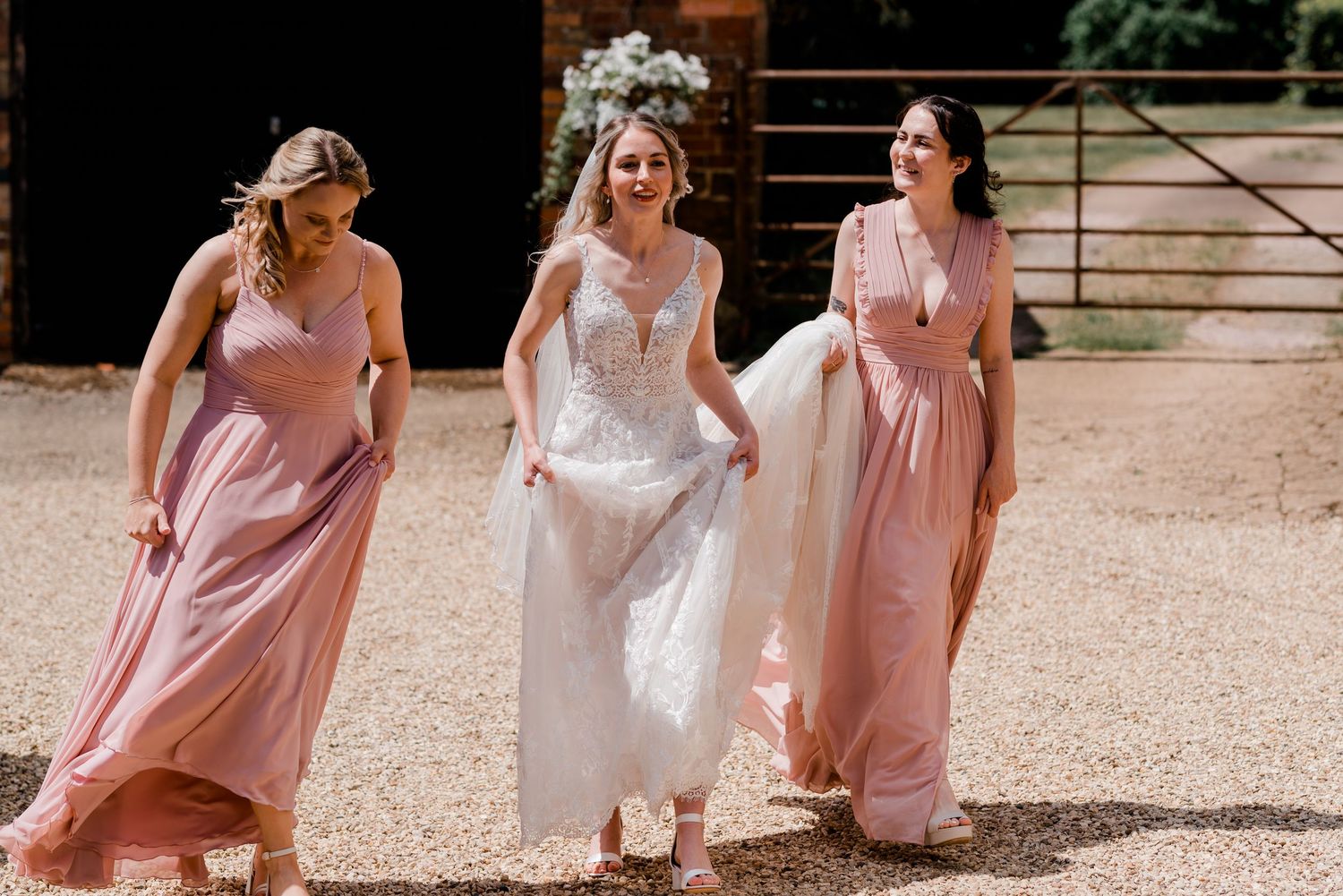 Wedding party members in pink dresses stand together in a sunlit garden setting.