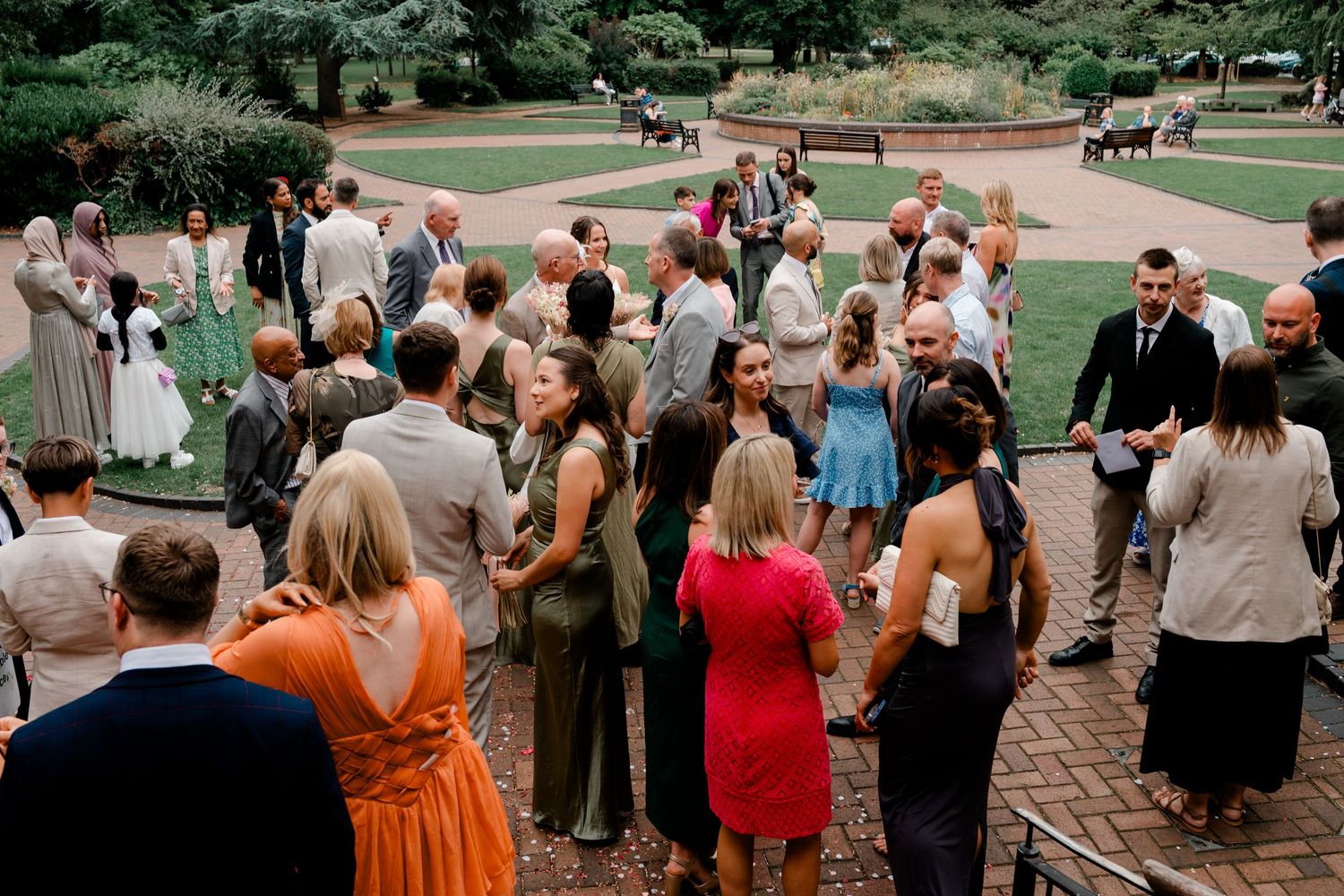 Guests mingling outdoors at a wedding reception in a lush garden setting with brick pathways.