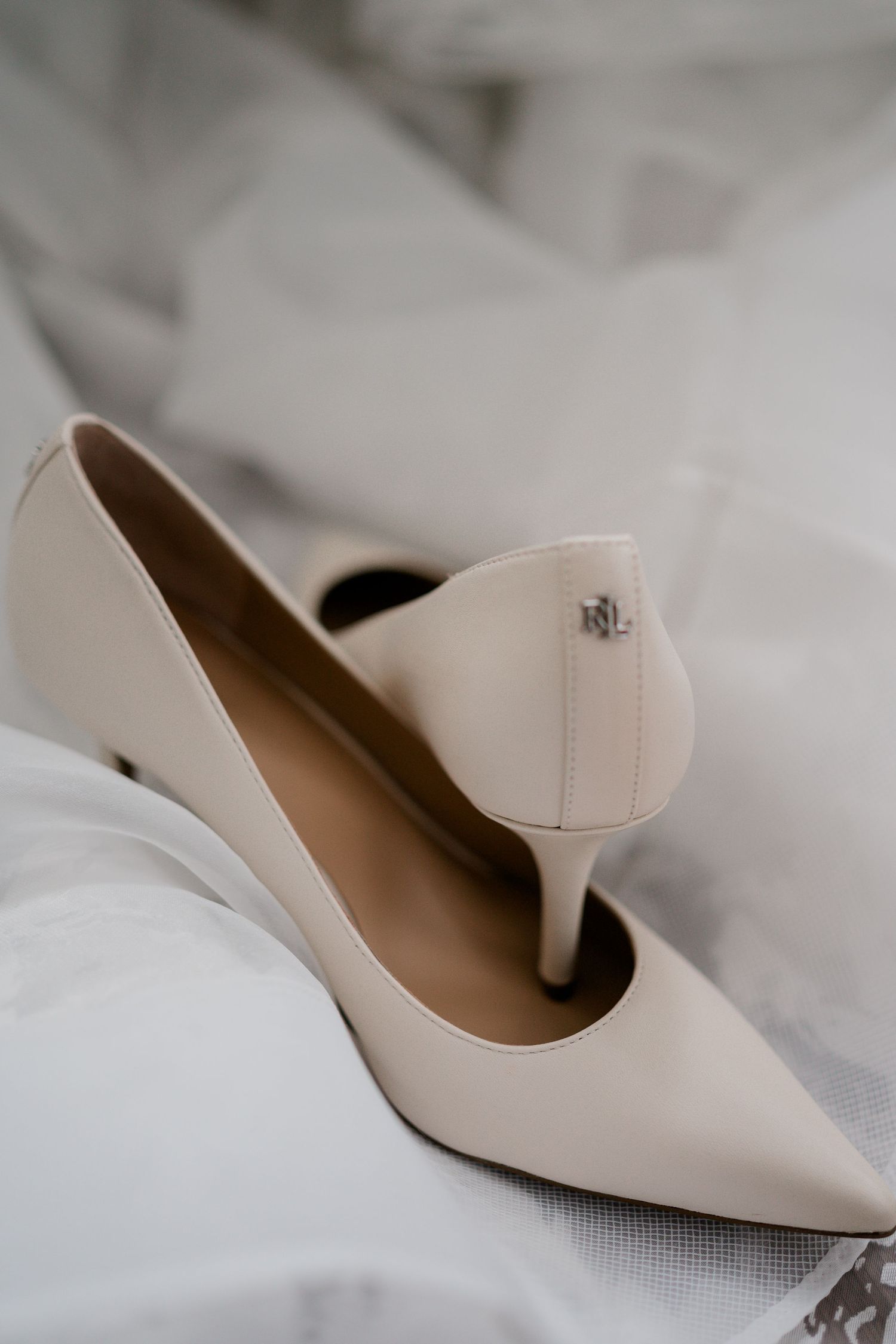 Elegant cream leather pointed-toe pumps by Ralph Lauren resting on white bridal fabric.