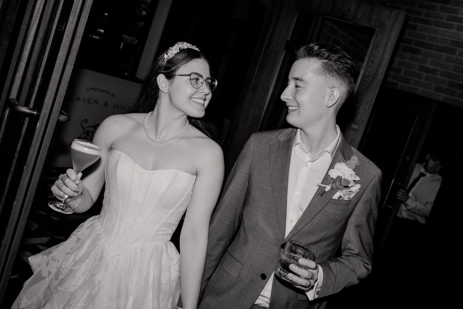Bride and groom share a joyful moment holding drinks at their wedding reception in black and white.
