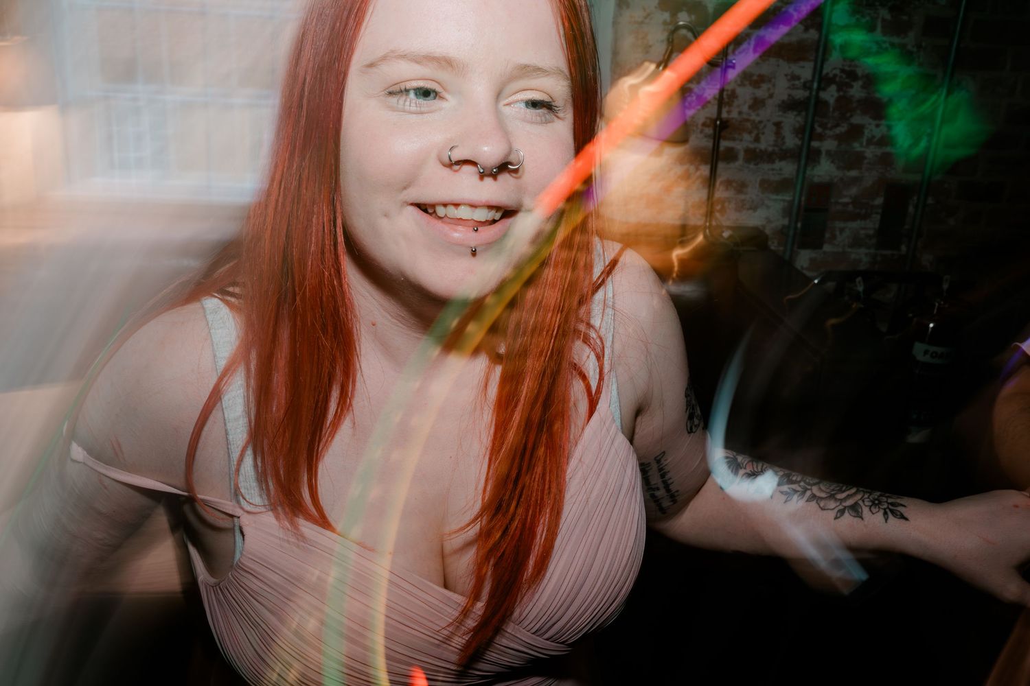 Young woman with red hair smiles surrounded by colorful light streaks at a party.