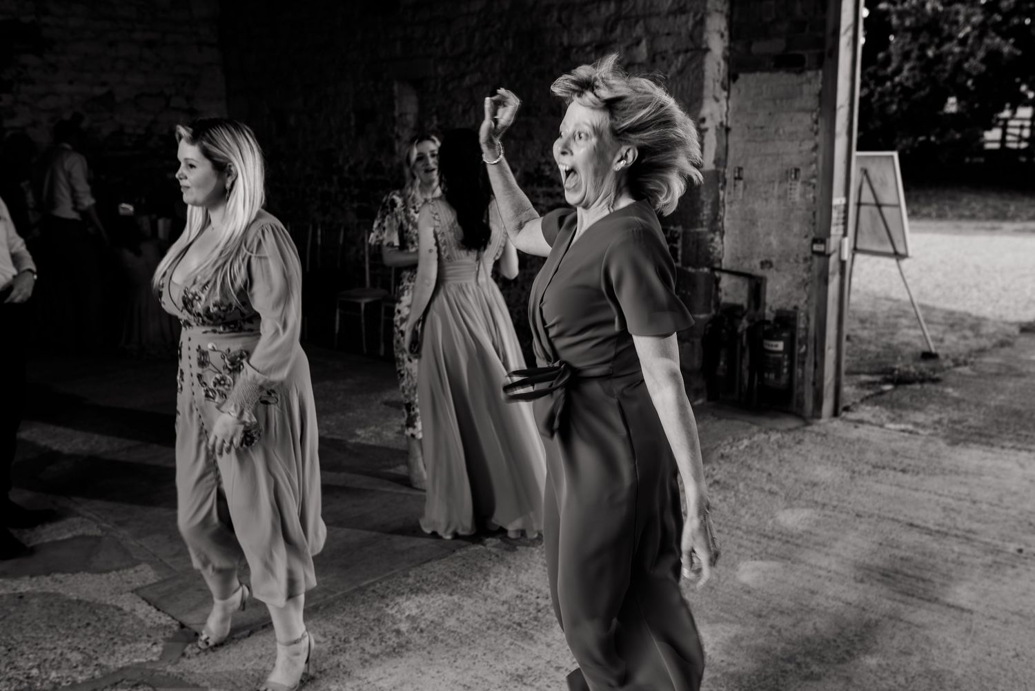 Black and white photo captures wedding guests socializing outside a rustic stone building.