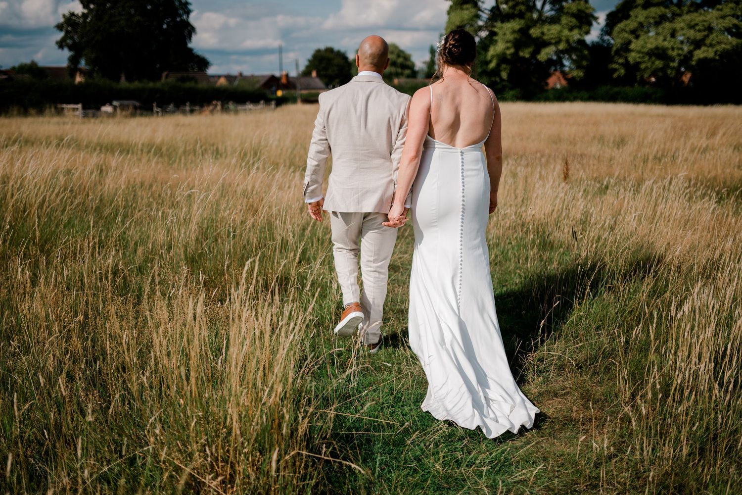 Couple walks through a scenic meadow with tall grass during their wedding day.