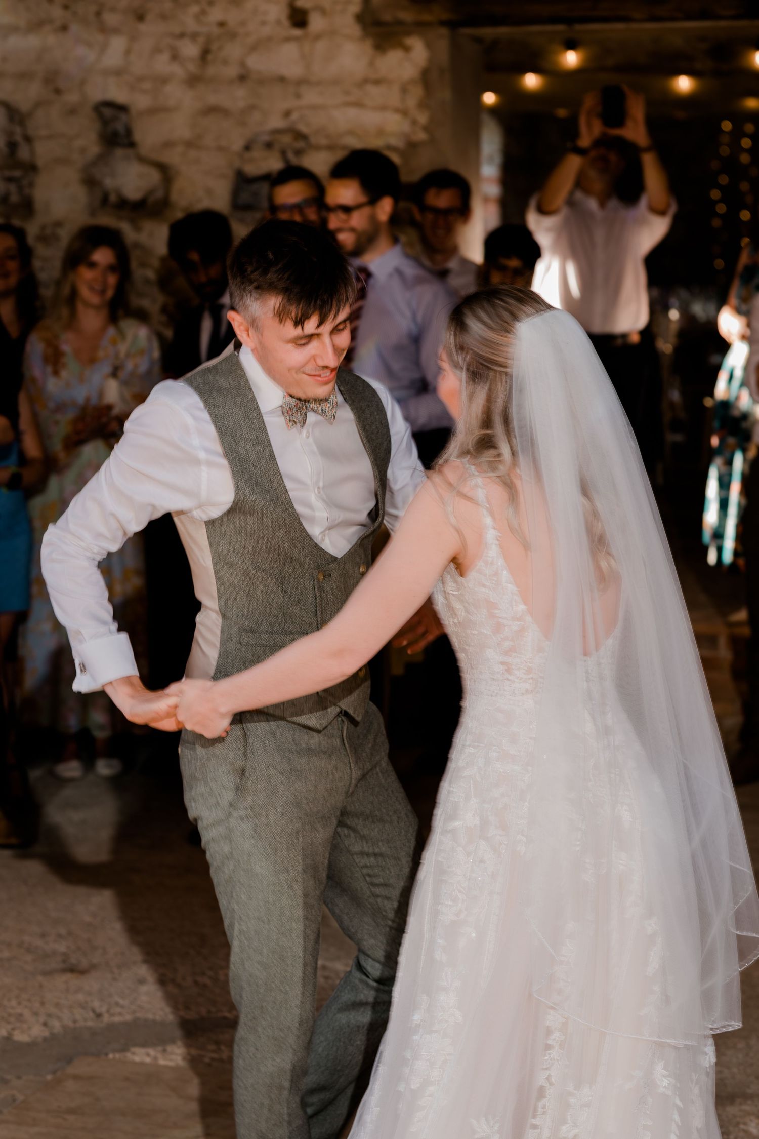 Guests dancing at a romantic evening barn reception with warm lighting and stone walls.
