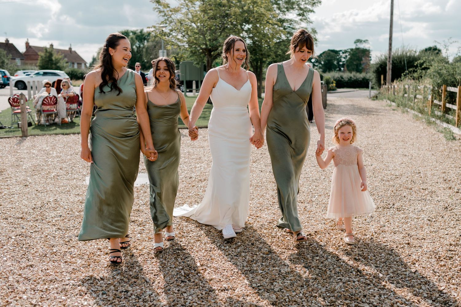 Wedding party walking together on gravel path in coordinated sage green and white attire.