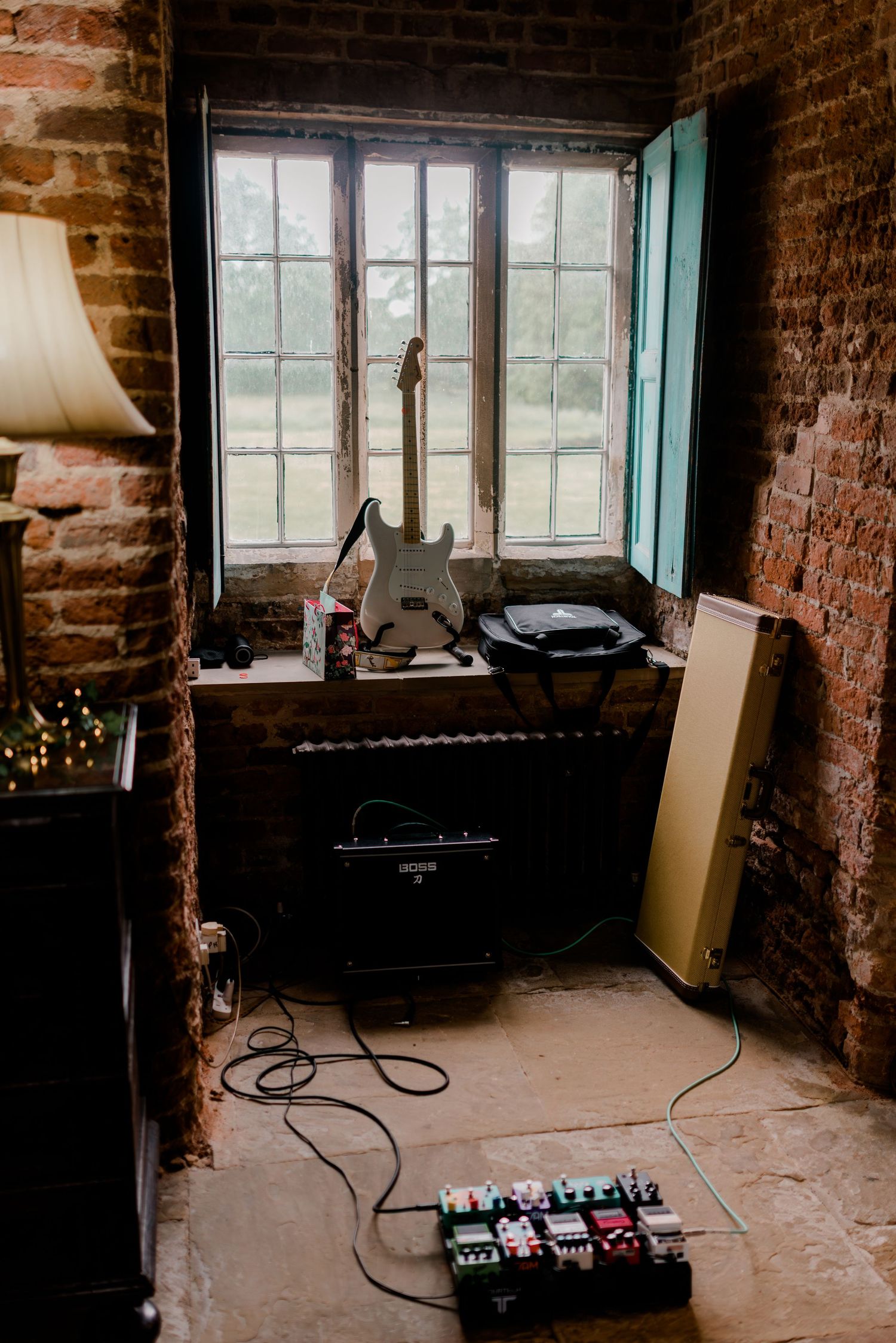 Guitar and music equipment set up by window in rustic brick room.