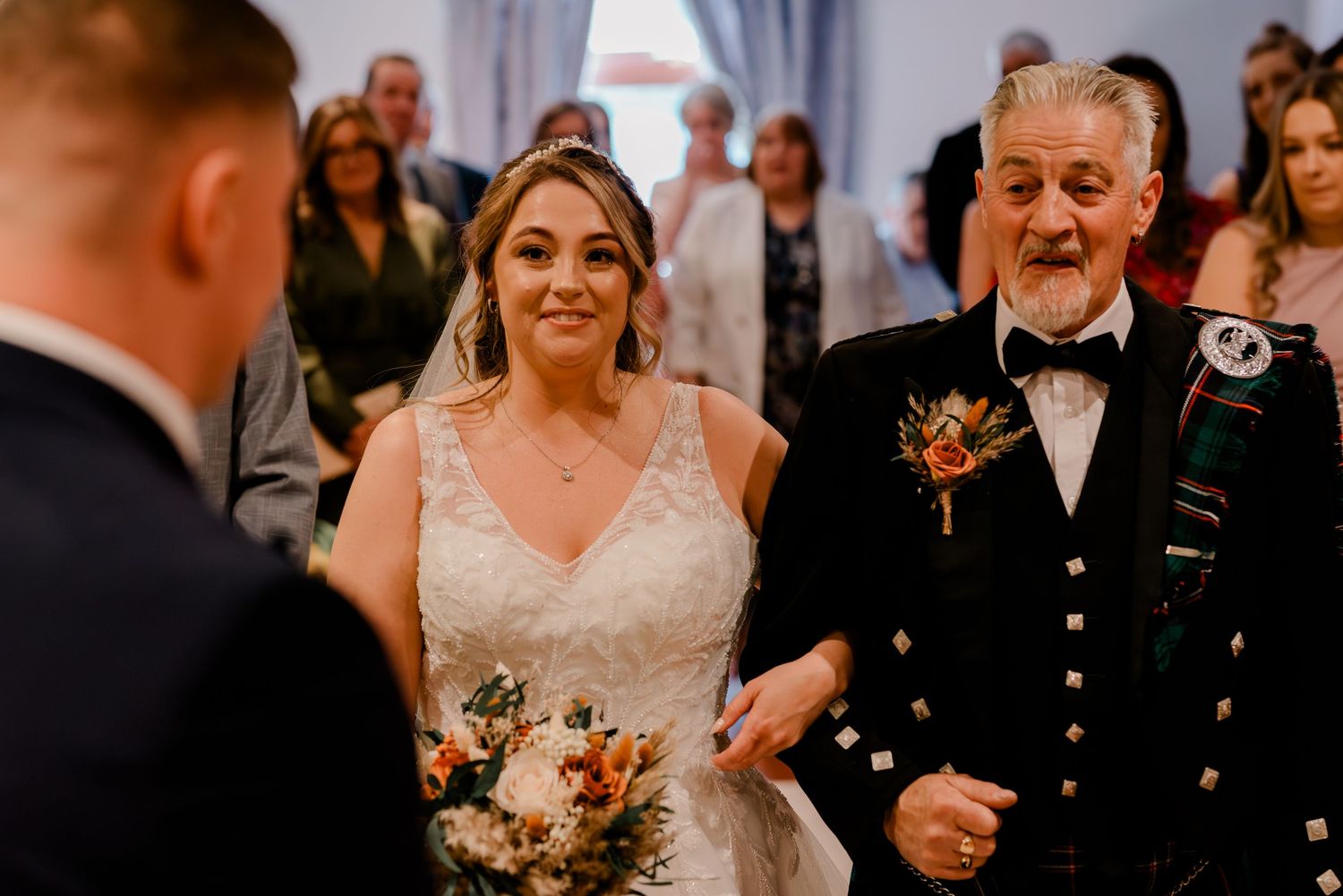 A traditional Scottish wedding ceremony showing the bride walking down the aisle with her father in his formal kilt.