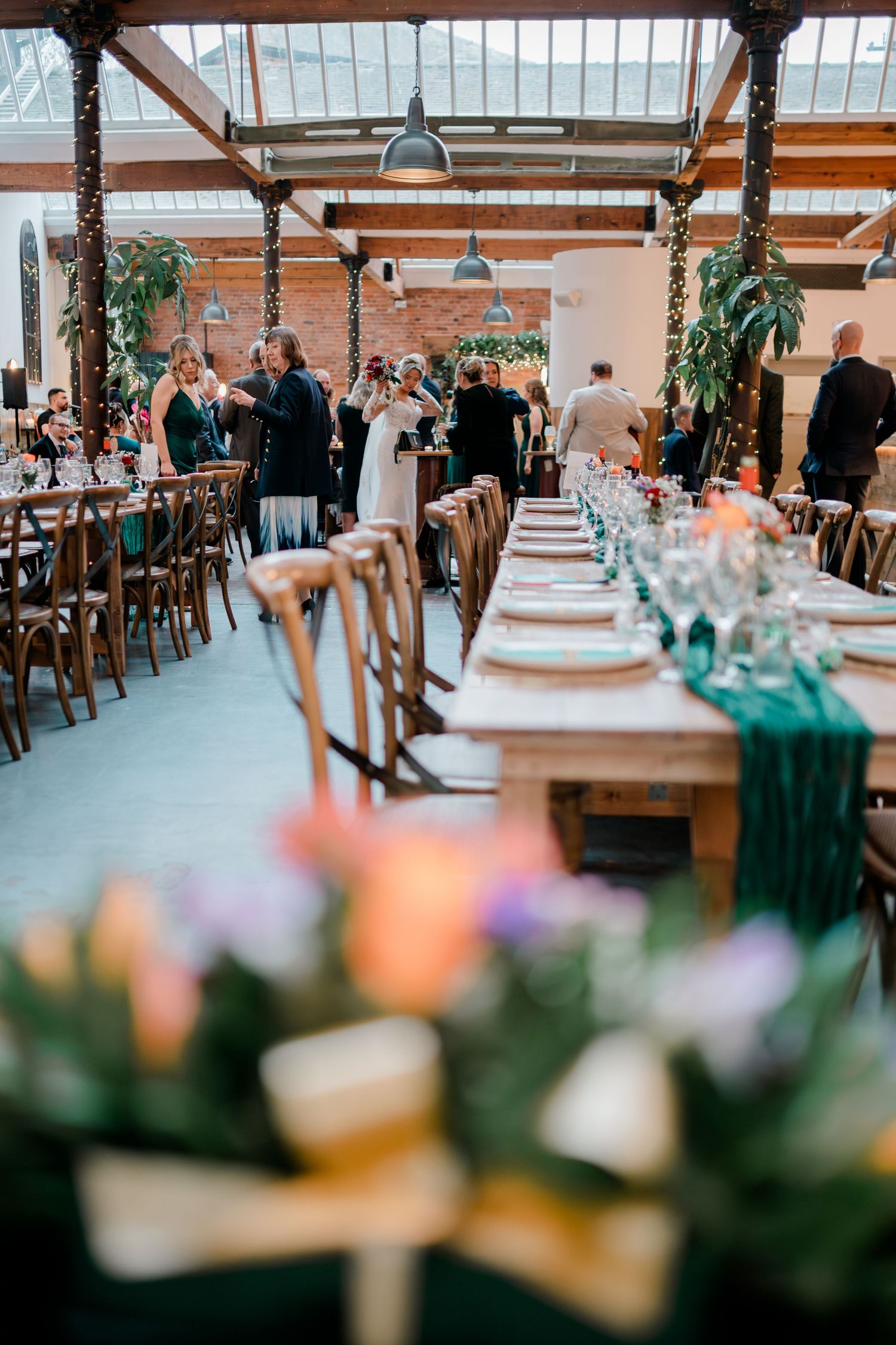 Elegant rustic wedding reception hall with long wooden tables, greenery and glass ceiling.