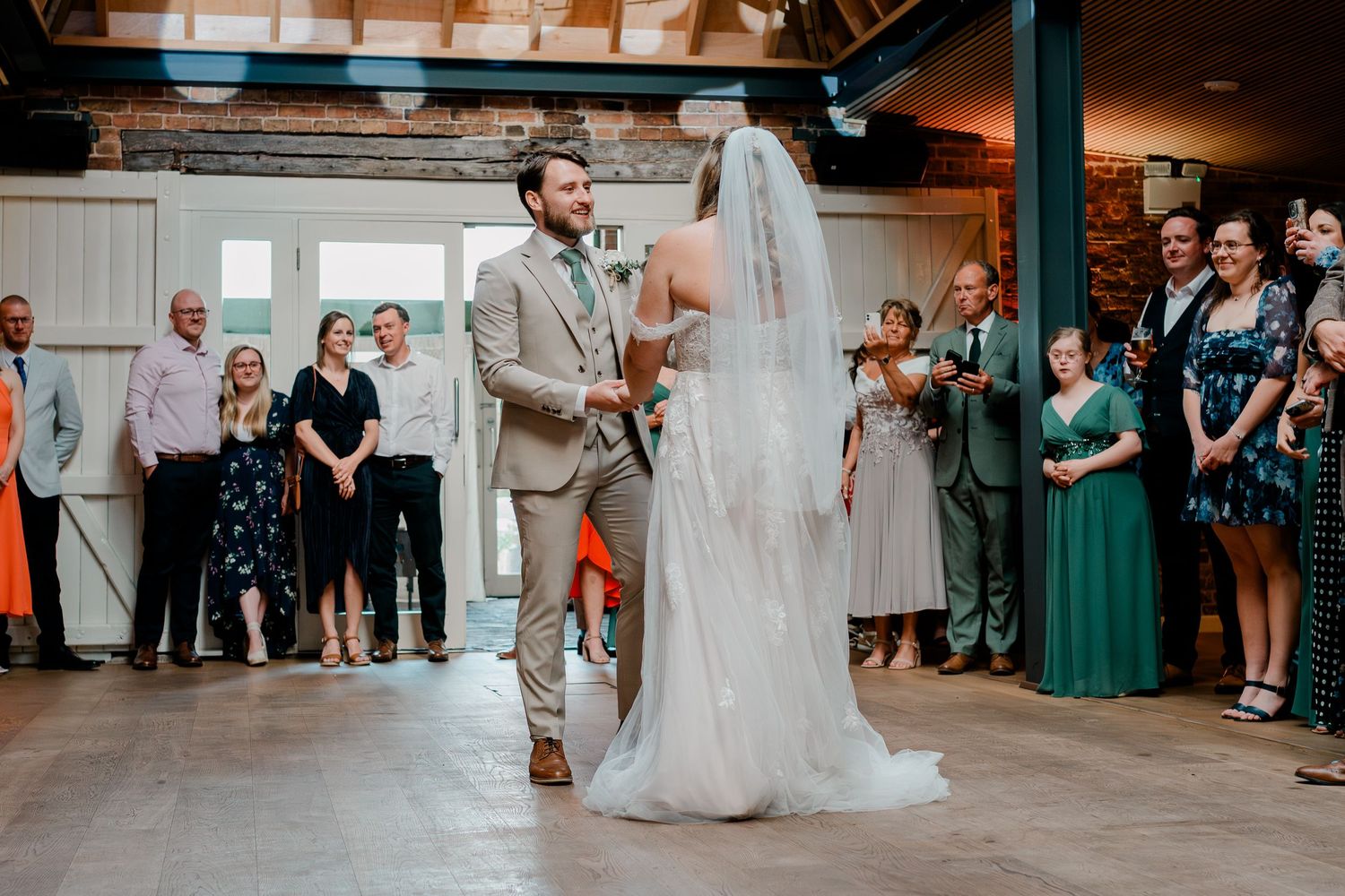 Bride and groom share first dance surrounded by guests in elegant rustic wedding venue.